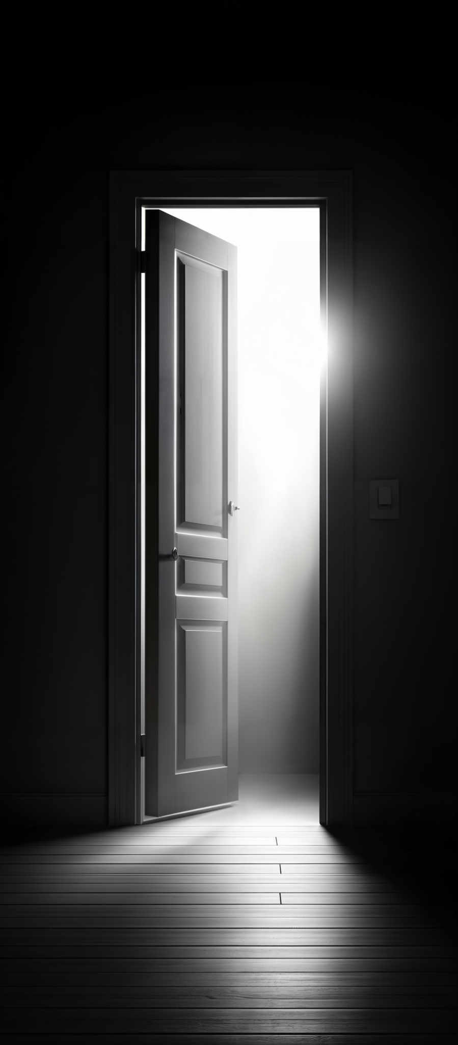 The image predominantly features monochromatic shades of black, white, and gray. The central focus is a door that is slightly ajar, revealing a bright light source outside. The door has a rectangular shape with multiple panels. The floor beneath the door appears to be made of wooden planks, and the walls are plain without any visible decorations. The light emanating from the door casts a shadow on the floor, creating a contrast between the illuminated and dark areas.