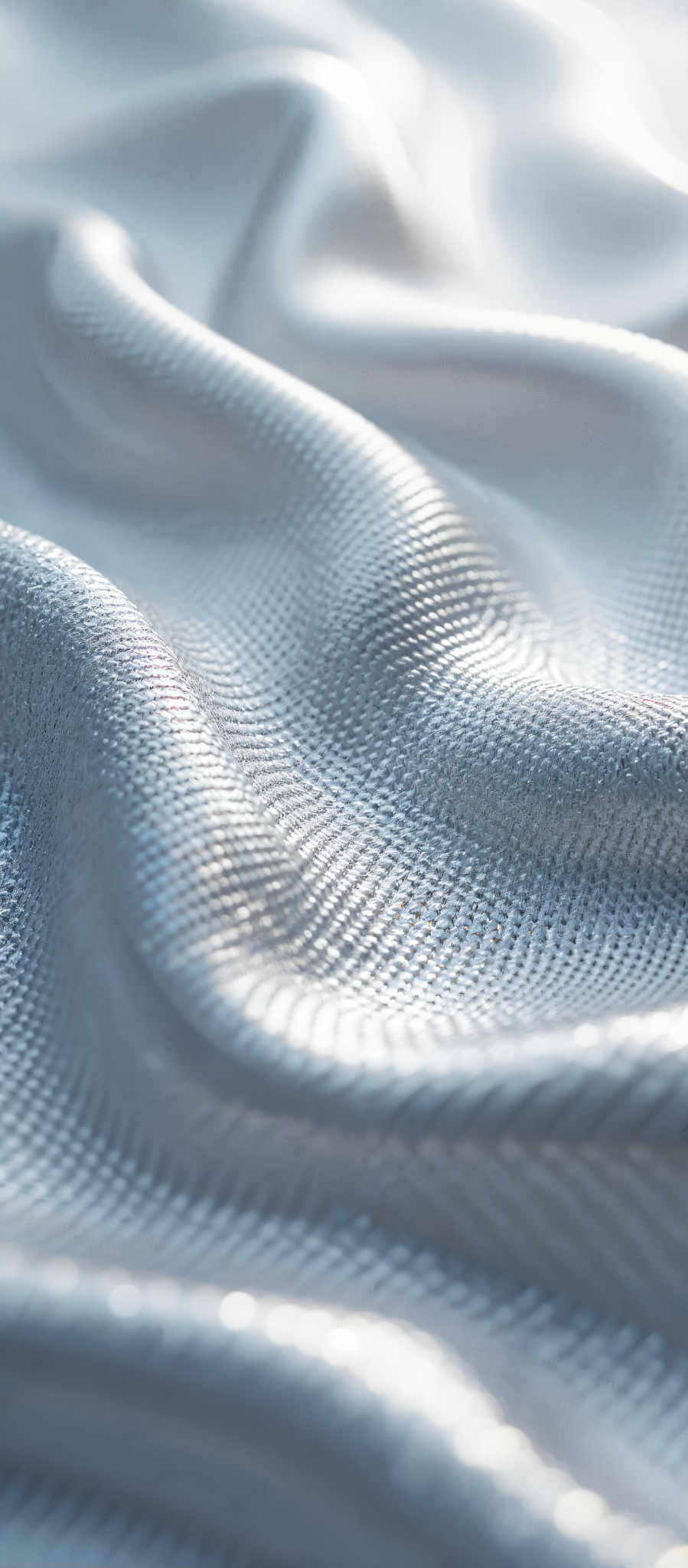 A close up of a shiny silver fabric. The fabric is made of small tightly woven threads that create a textured surface. The light reflects off the fabric giving it a shiny appearance. The image is taken from a slightly angled perspective adding depth to the scene. The focus is on the fabric's texture and the way the light interacts with it. The color is a bright silver and the fabric appears to be made of a metallic material. The overall effect is a shiny textured surface that catches the light.