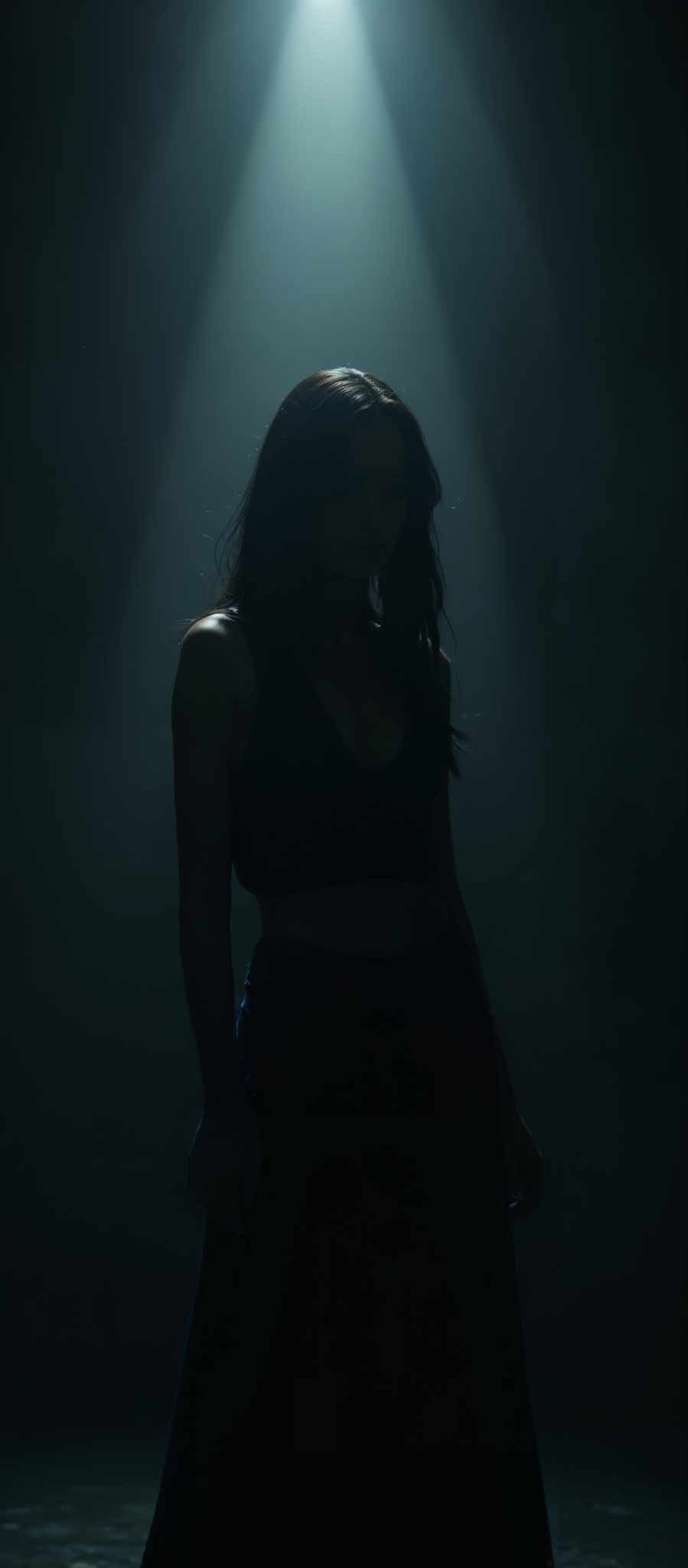 A woman with long dark hair stands in a dimly lit room. She is wearing a black tank top and black shorts. The room is illuminated by a single light source casting a dramatic shadow on her face. The background is dark creating a stark contrast with the woman's figure. The overall mood of the image is mysterious and moody. The colors are predominantly black and gray with hints of blue and green in the background. The art style is dramatic and moODY with a focus on the woman as the subject. The motif is a sense of solitude and introspection.