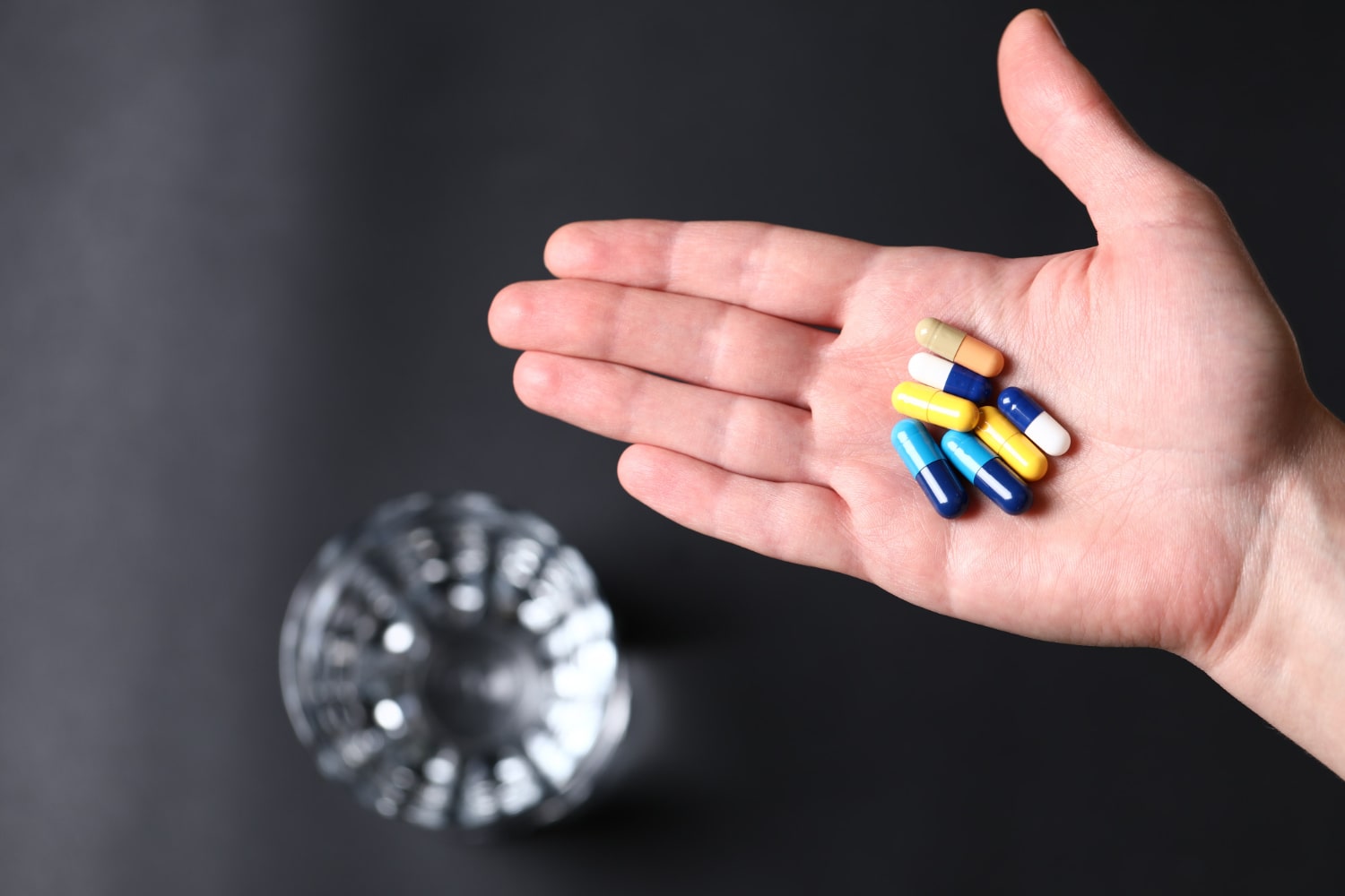 colorful medical pills in the hand of a person and a glass of water