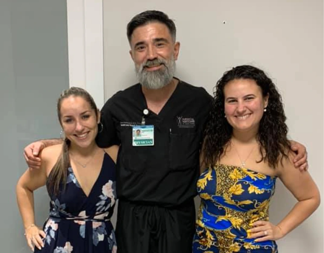 Bariatric surgeon in black scrubs smiling with two patients in our South Miami office hallway