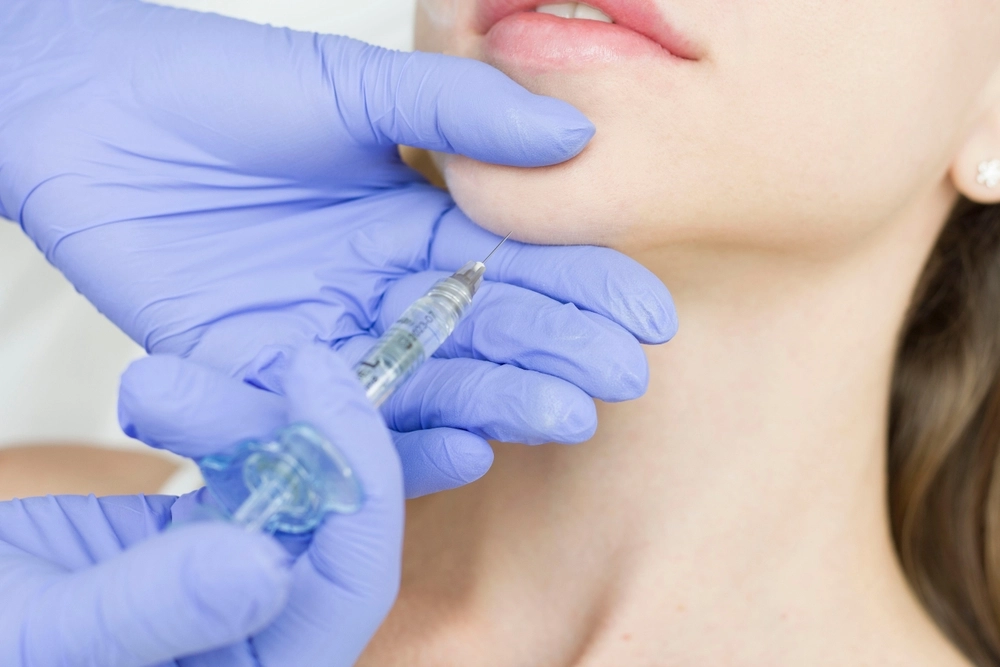 A gloved provider injects dermal filler into a woman's chin during a cosmetic procedure