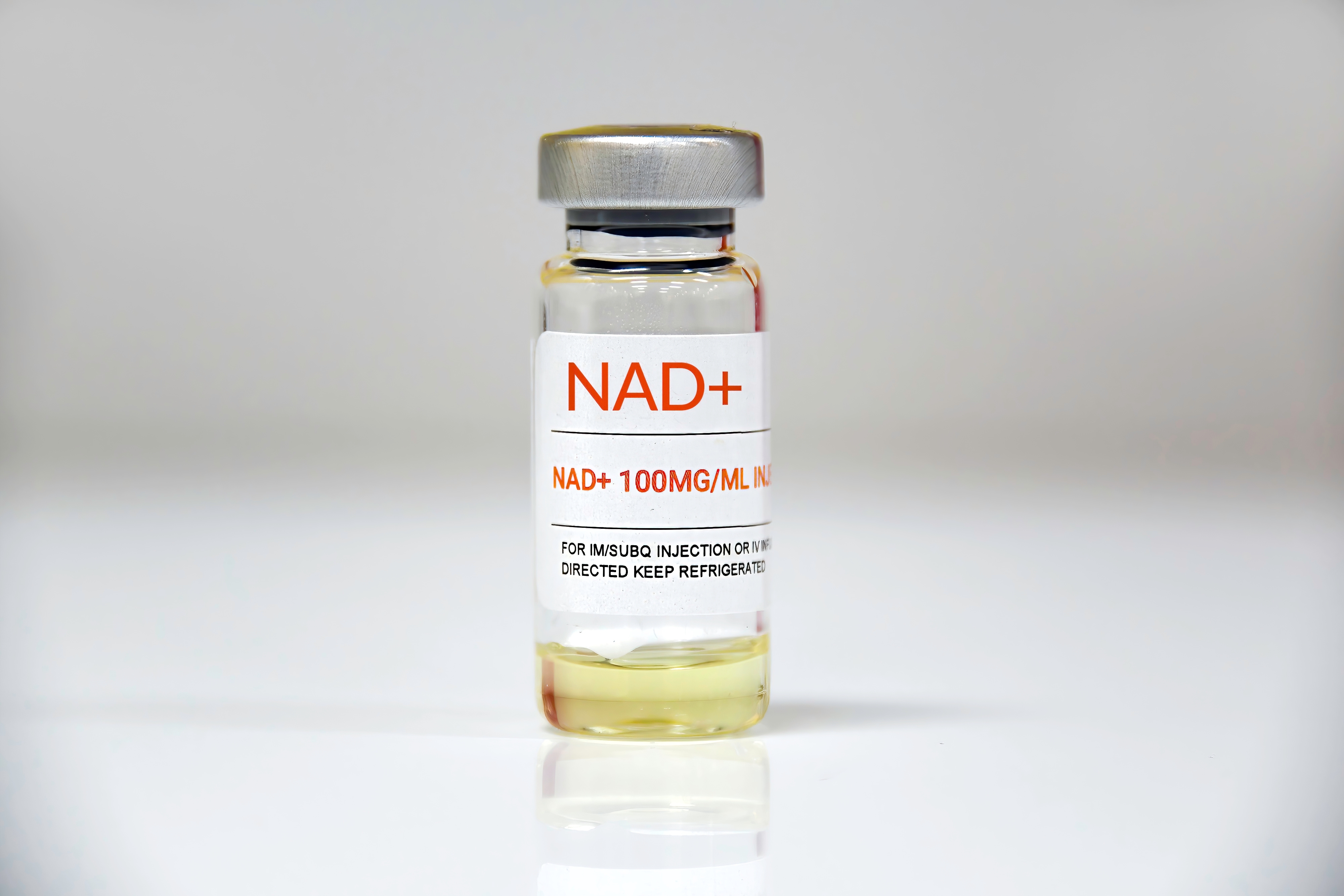A glass vial of injectable NAD+ with a silver cap on a white surface