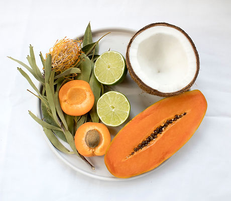 Plate of fresh papaya, coconut, lime and apricot halves with green leaves