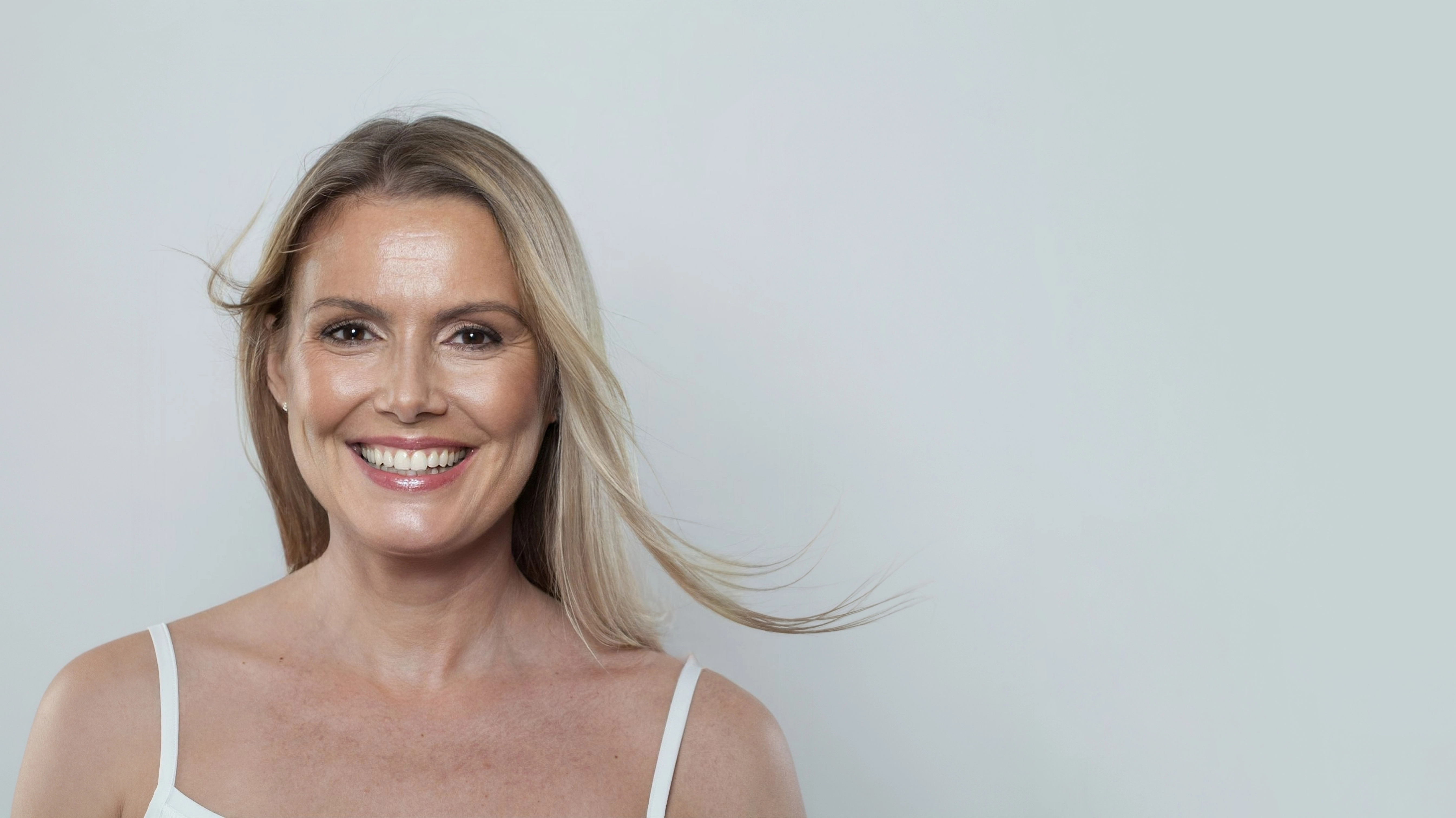 Studio headshot of a smiling middle-aged woman with flowing blonde hair, used to illustrate hormone optimization therapy on t