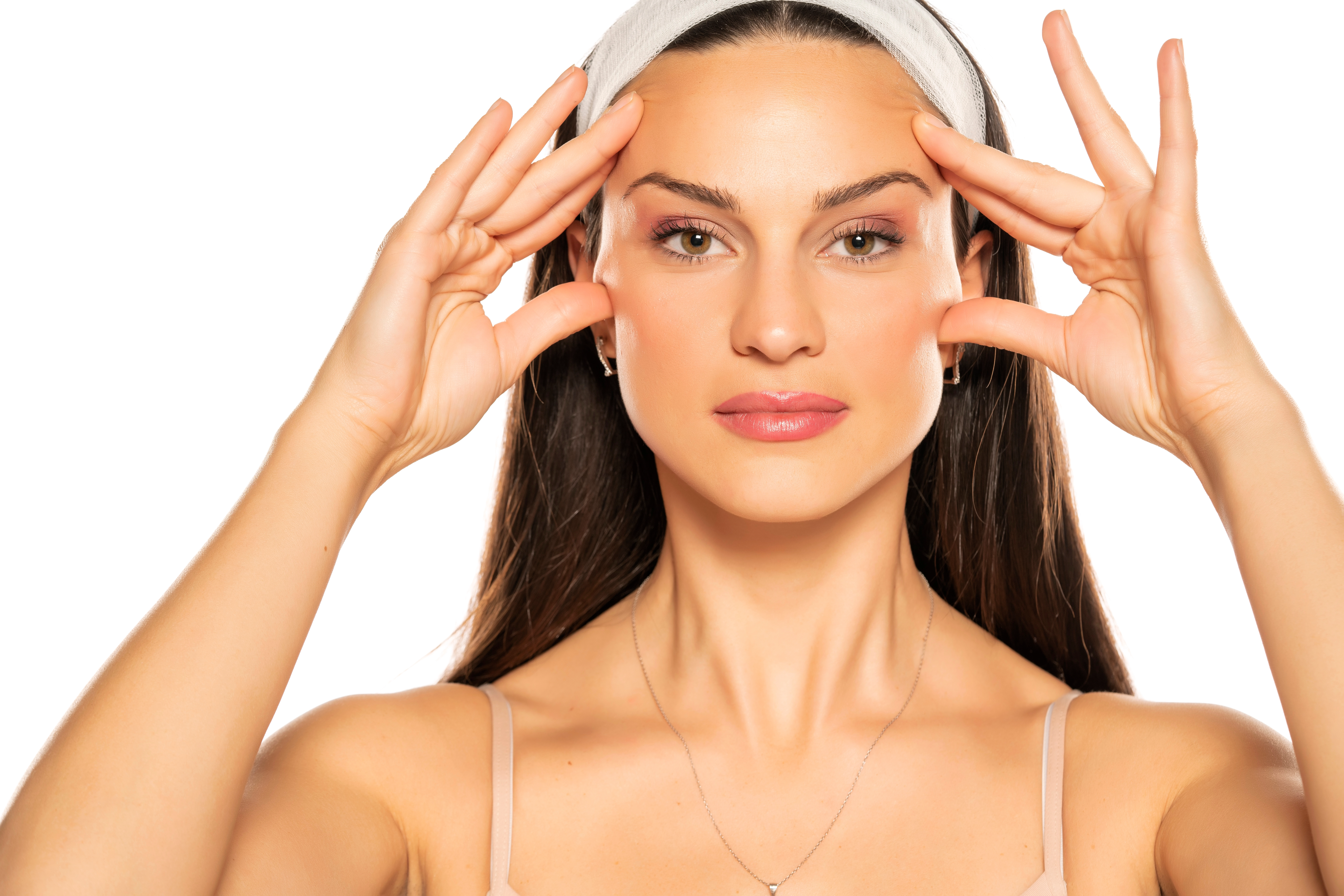 A woman with a headband touches her face with both hands, showcasing smooth, tightened facial skin