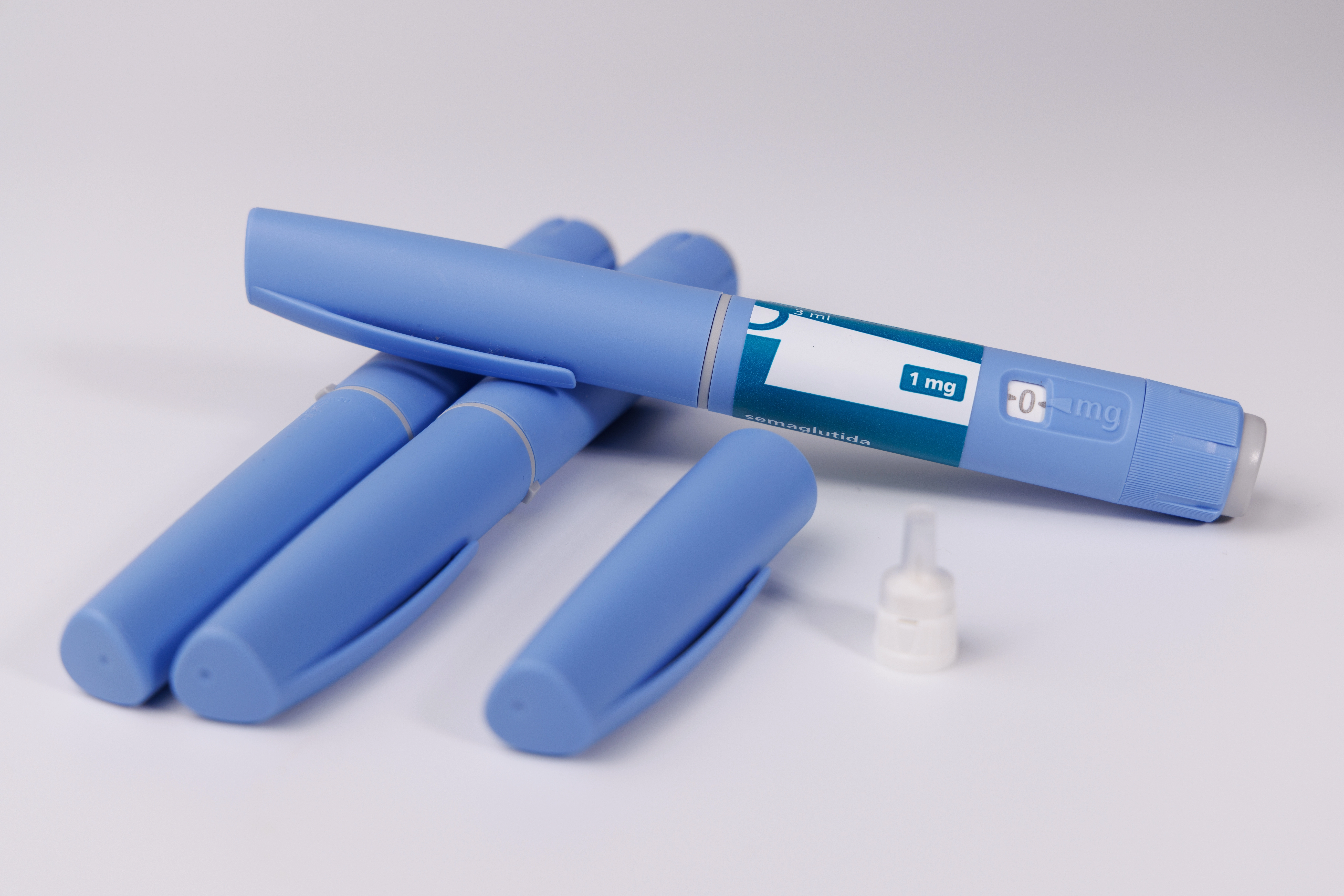 Several blue semaglutide injector pens with a needle tip lying on a white surface