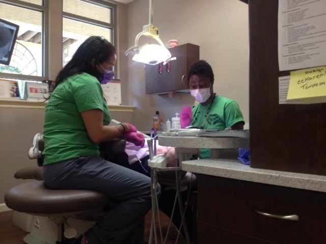 Two staff members in green scrubs and masks working with a patient in a dental chair during a 'Smiles that care' community ev