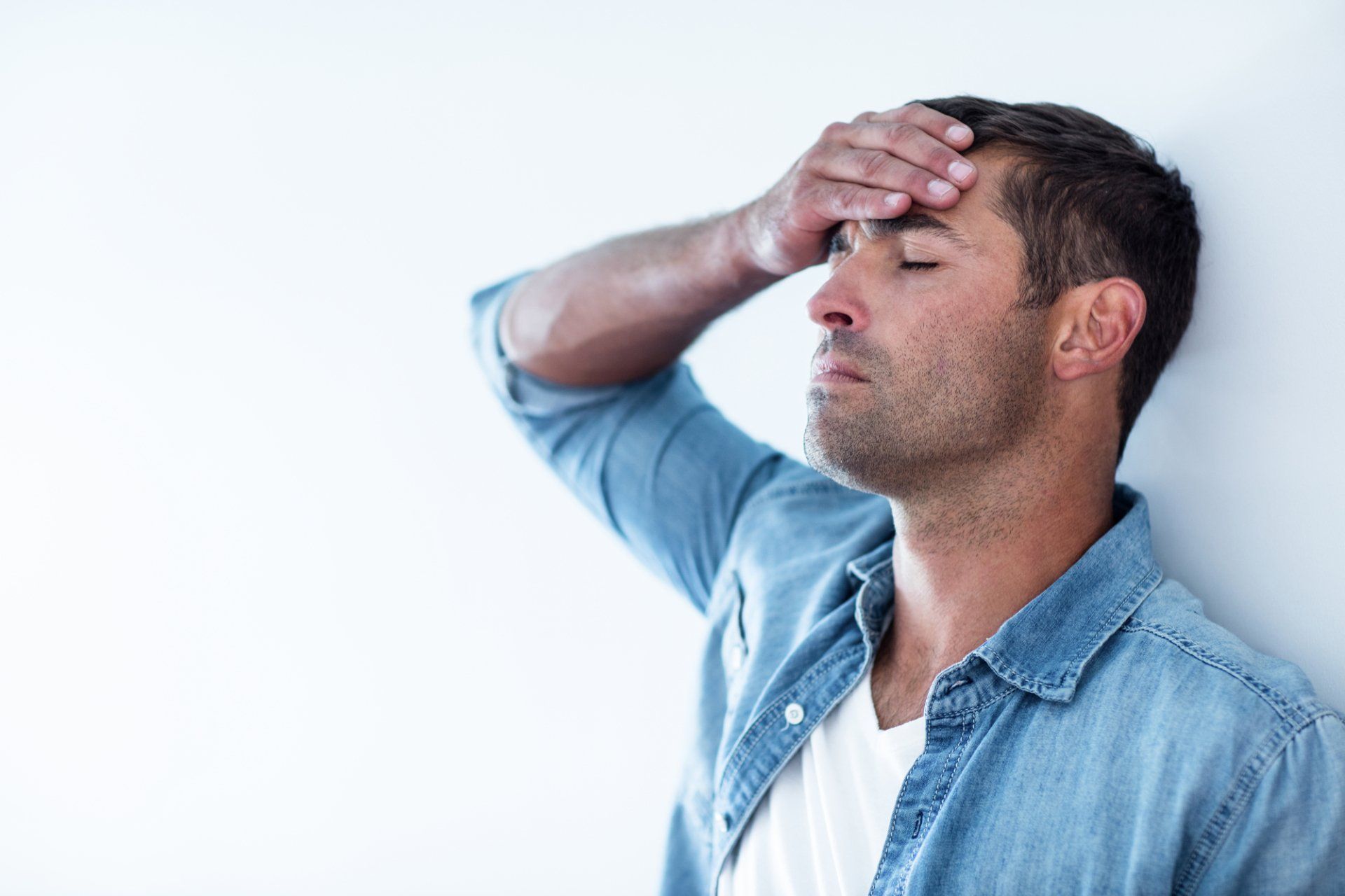 A stock photo of a man with his eyes closed and hand on his forehead, used to illustrate symptoms related to conditions treat