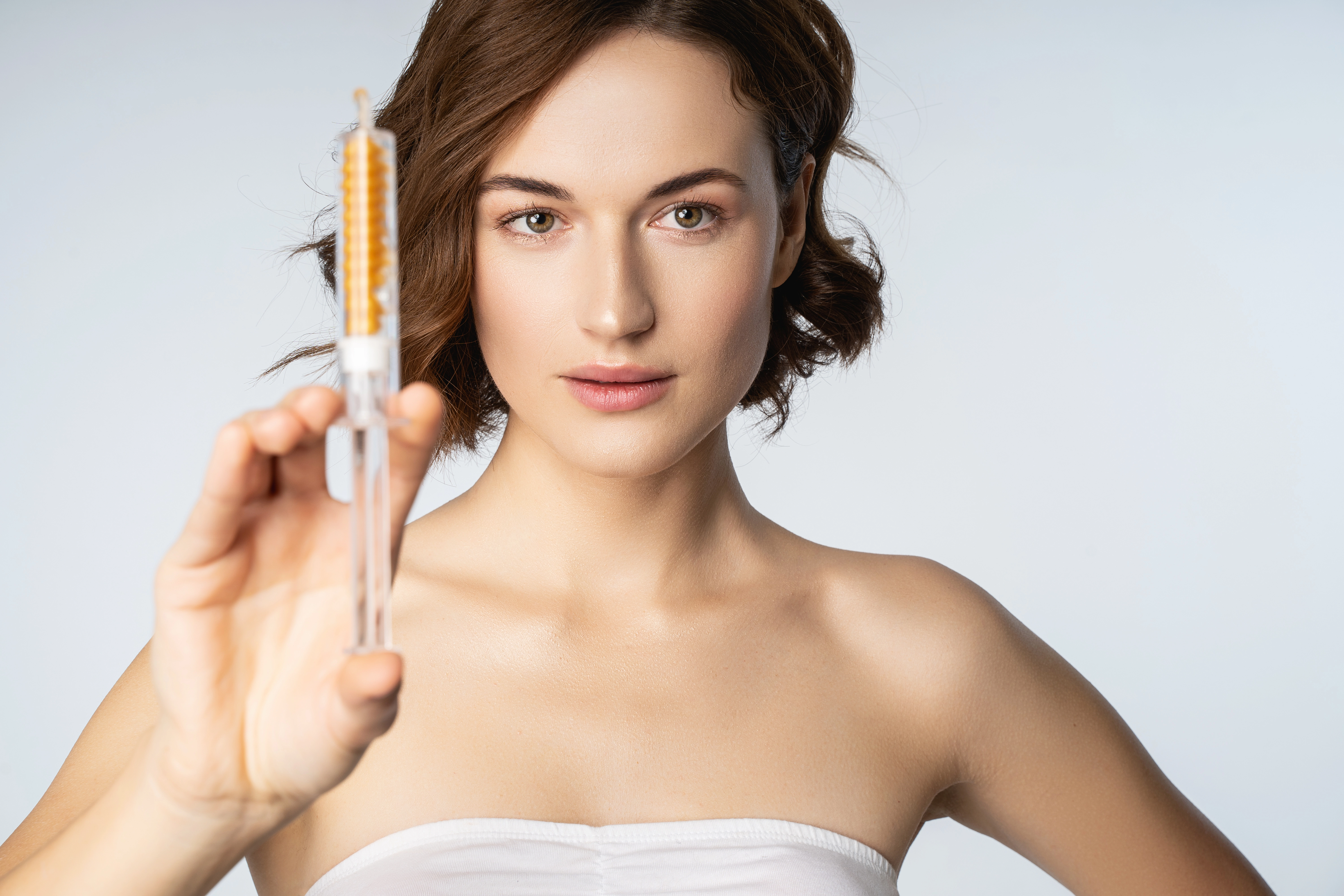 A woman with clear skin holds up a syringe filled with amber liquid, representing a B12 injection treatment.