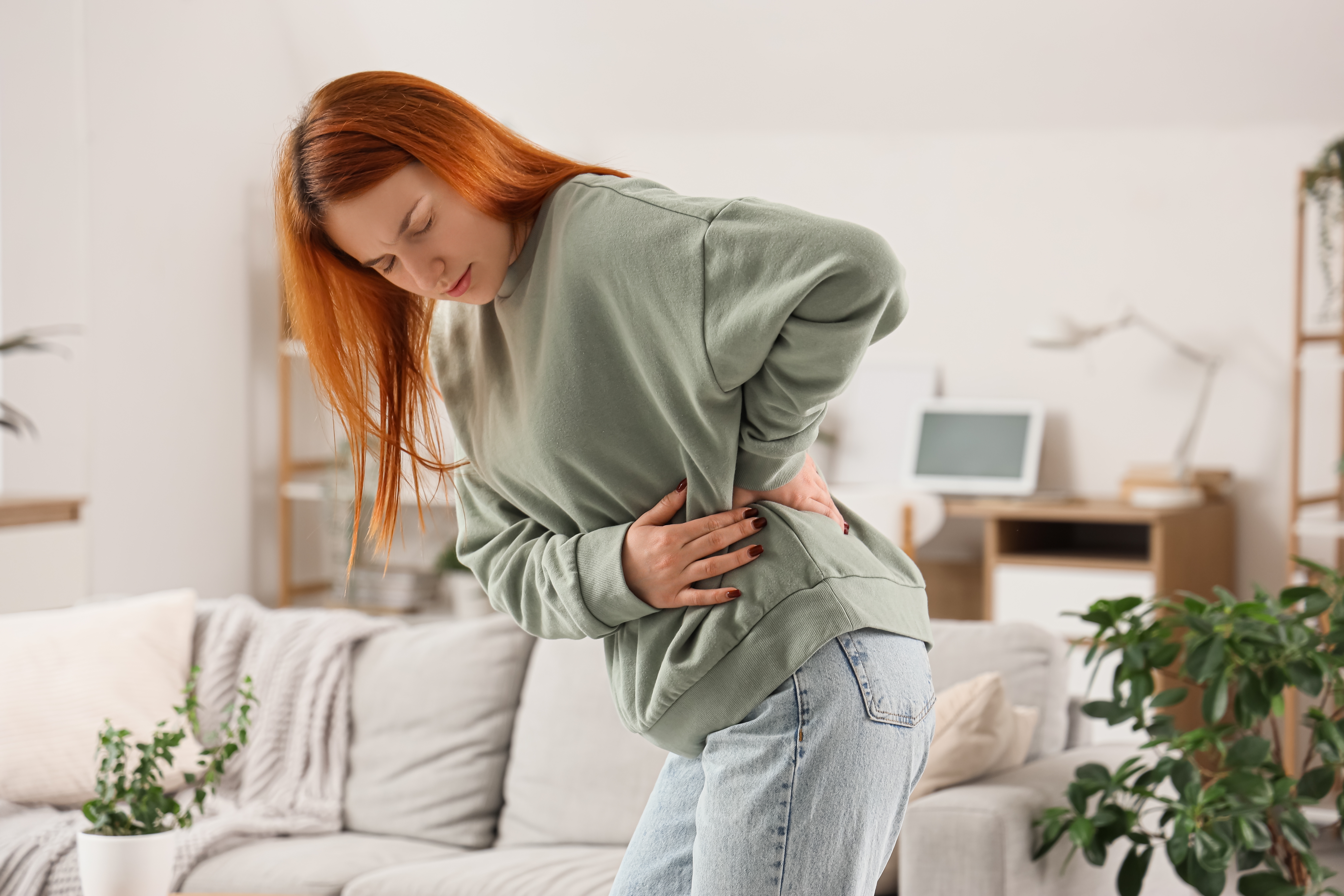 Woman at home holding her lower back and abdomen in discomfort