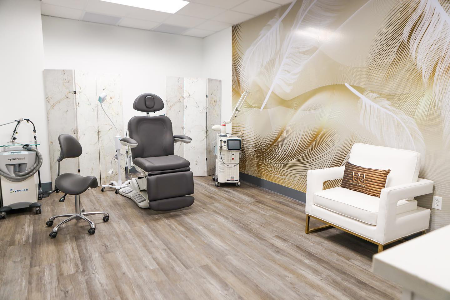 Procedure room at VIA Health & Medspa in Chandler with a treatment chair, laser devices and a gold feather wall mural