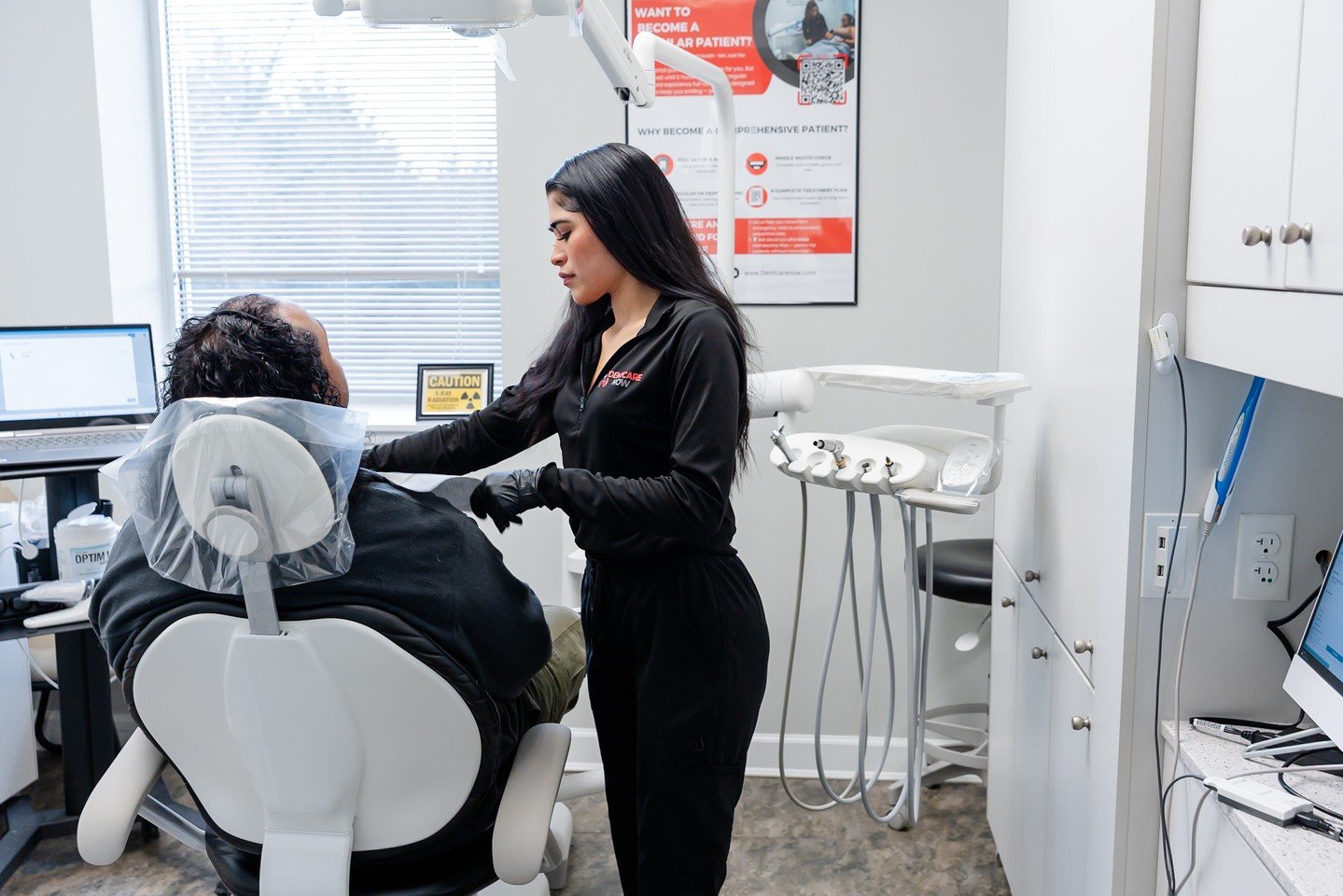 A dental staff member in black scrubs treats a male patient in a dental chair during an emergency same-day appointment at the