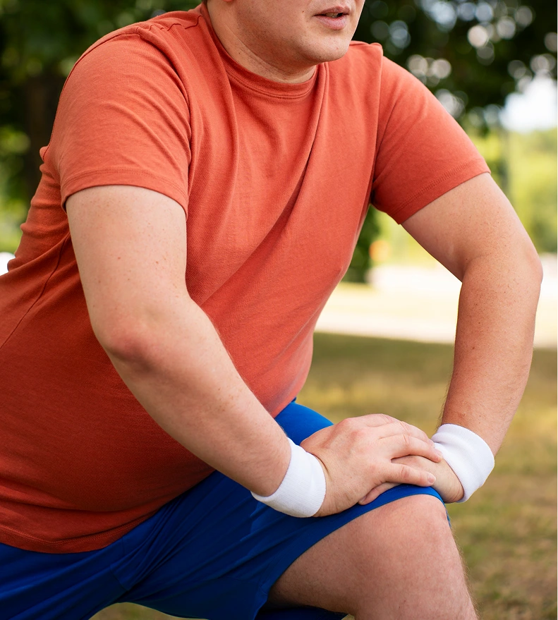 Man in athletic wear pausing to stretch his knee during an outdoor walk