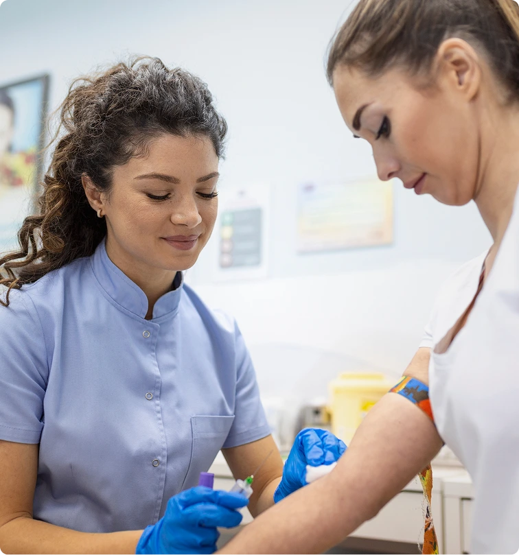A nurse in blue scrubs draws blood from a patient's arm in a clinical office setting.