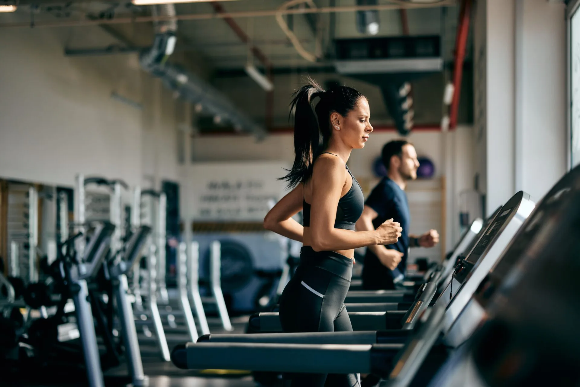 Woman and man running on treadmills in a bright gym, a cardio workout that supports healthy blood vessels