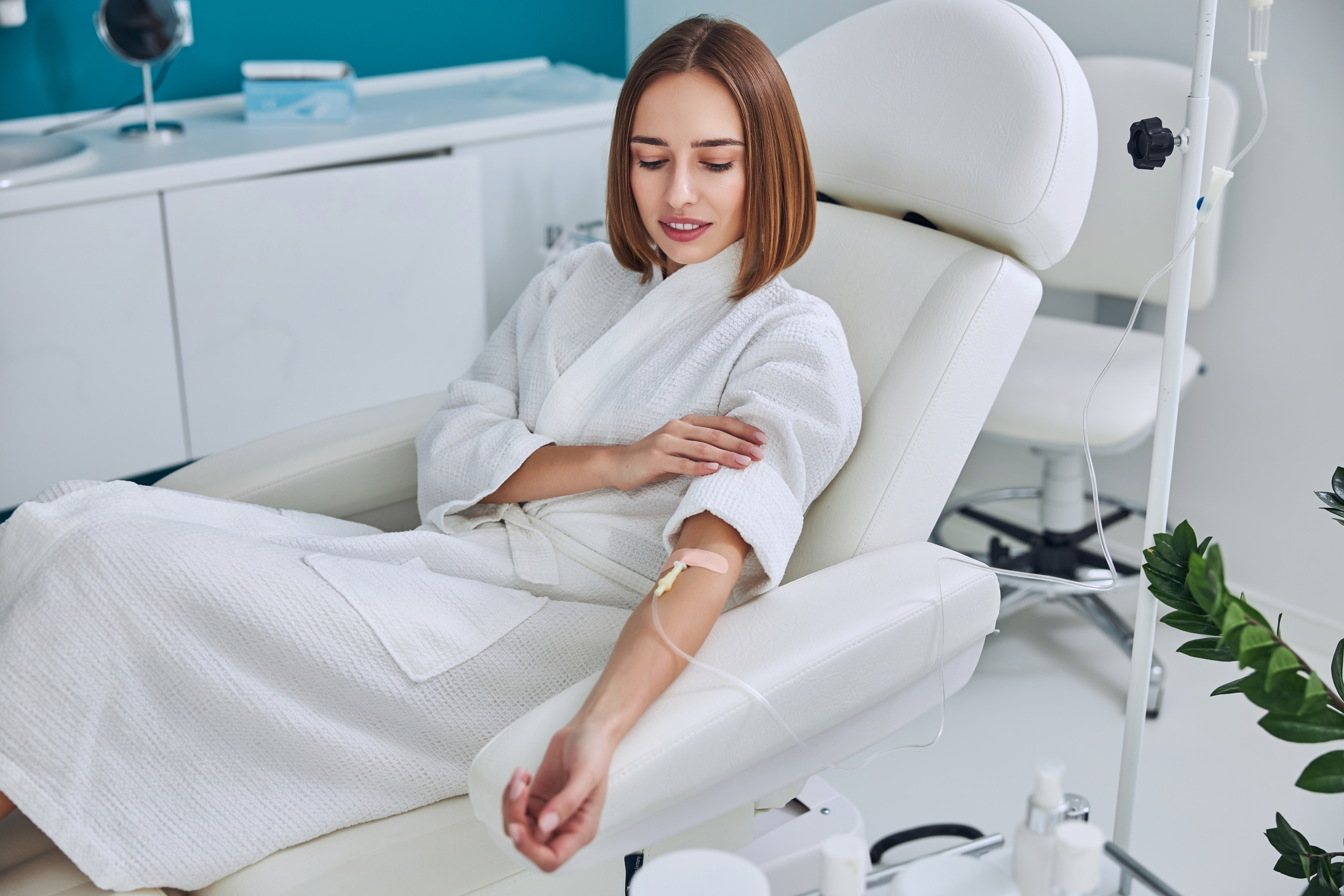 Woman in a white robe resting in a reclining treatment chair while receiving an IV drip