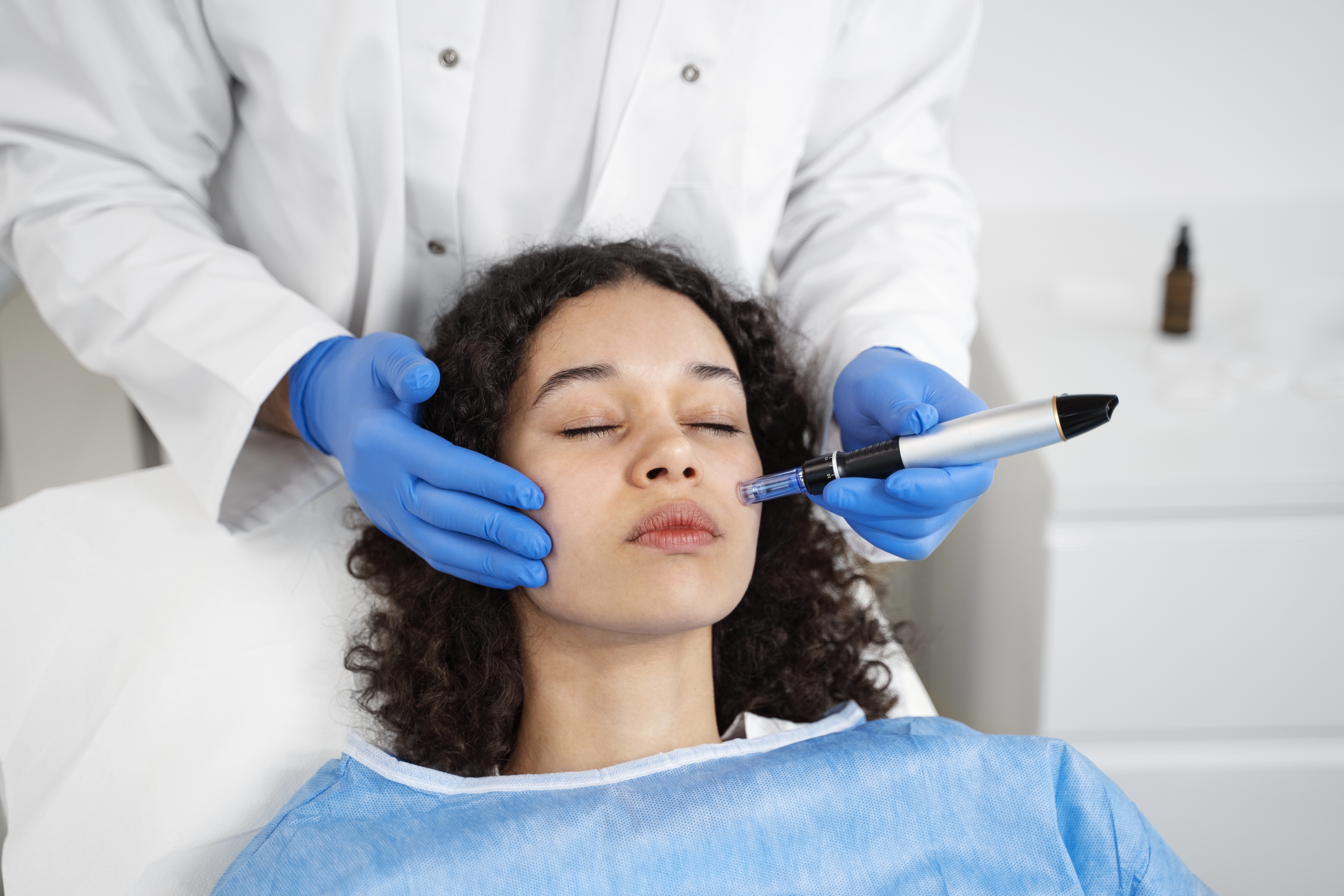 Microneedling pen moving across a woman's cheek during a facial collagen induction treatment