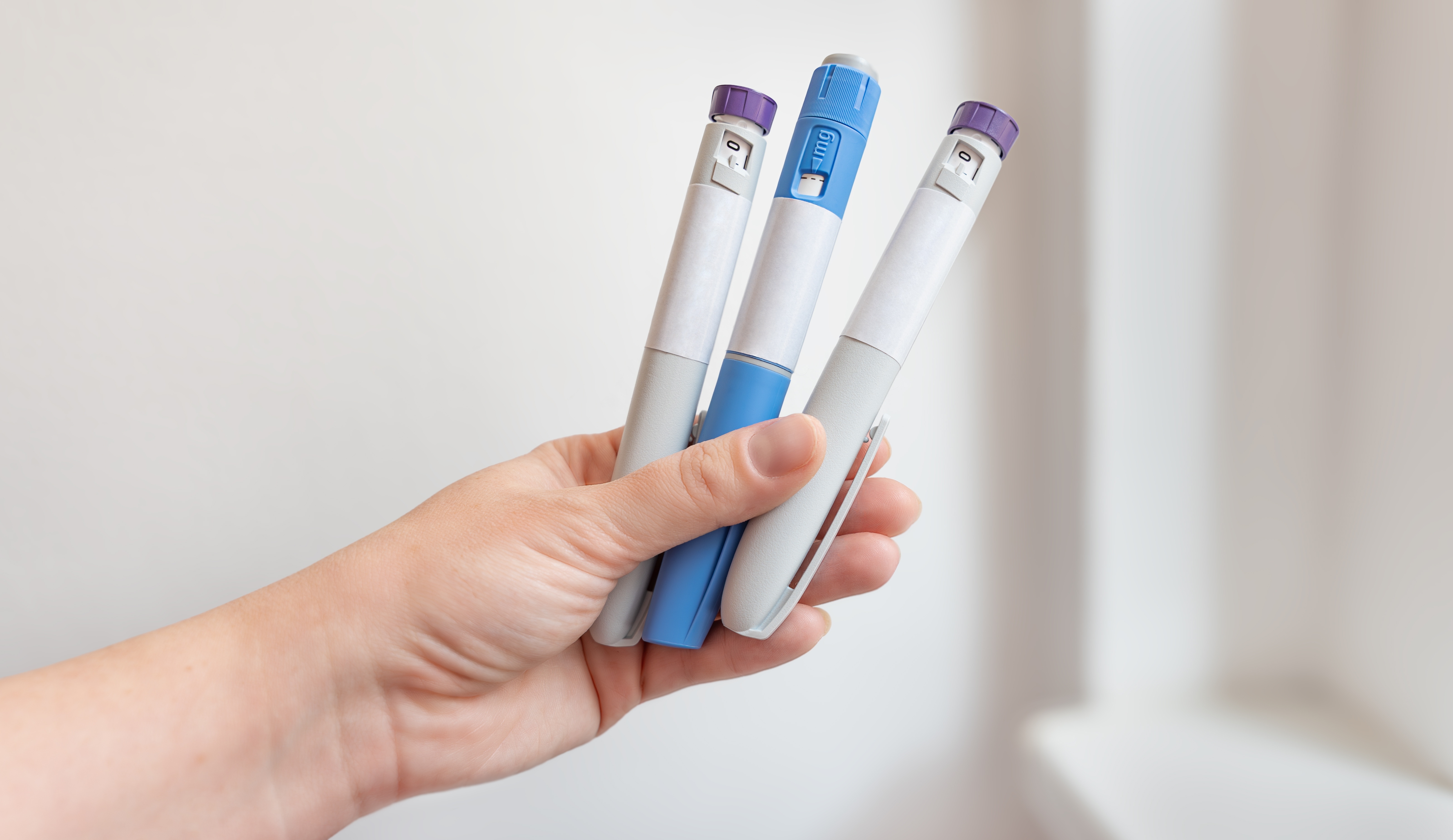 A hand holding three injectable pens used for medical weight loss