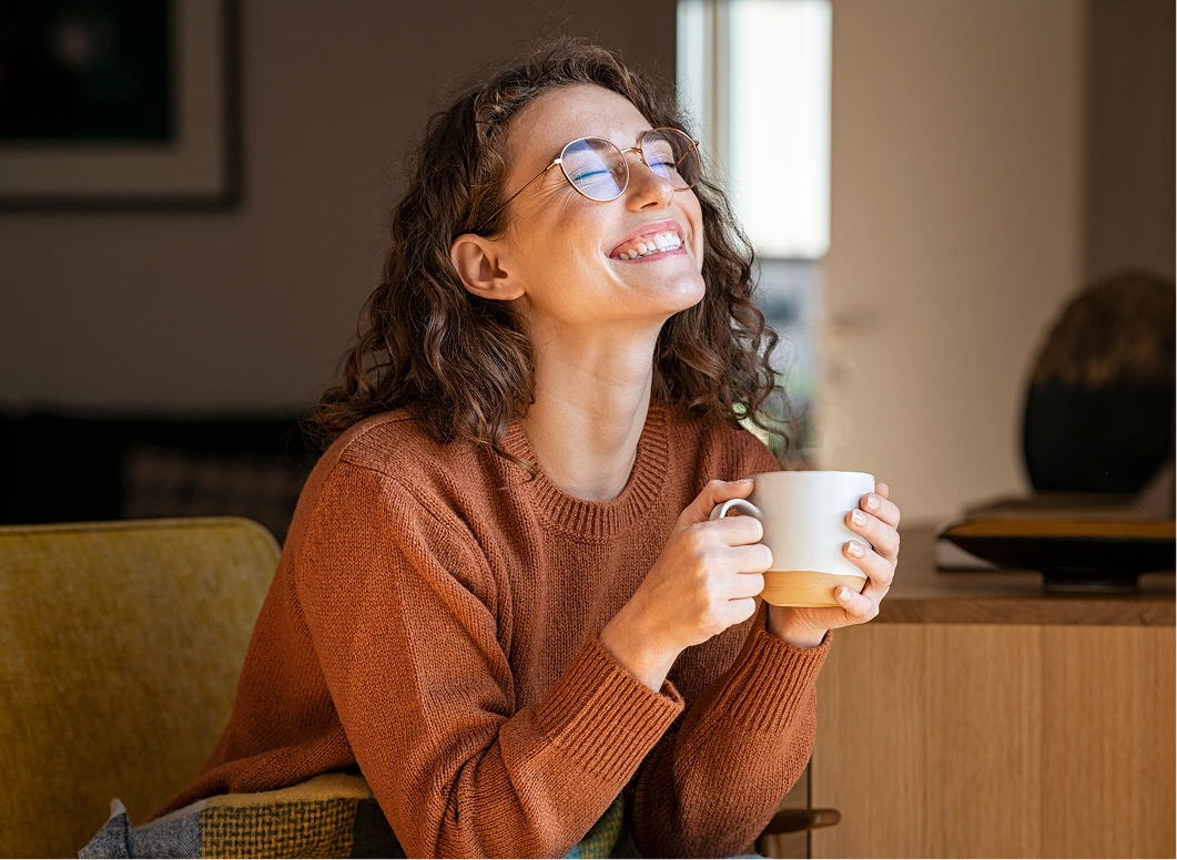 Smiling woman in a rust sweater holding a warm mug, relaxed at home in soft window light