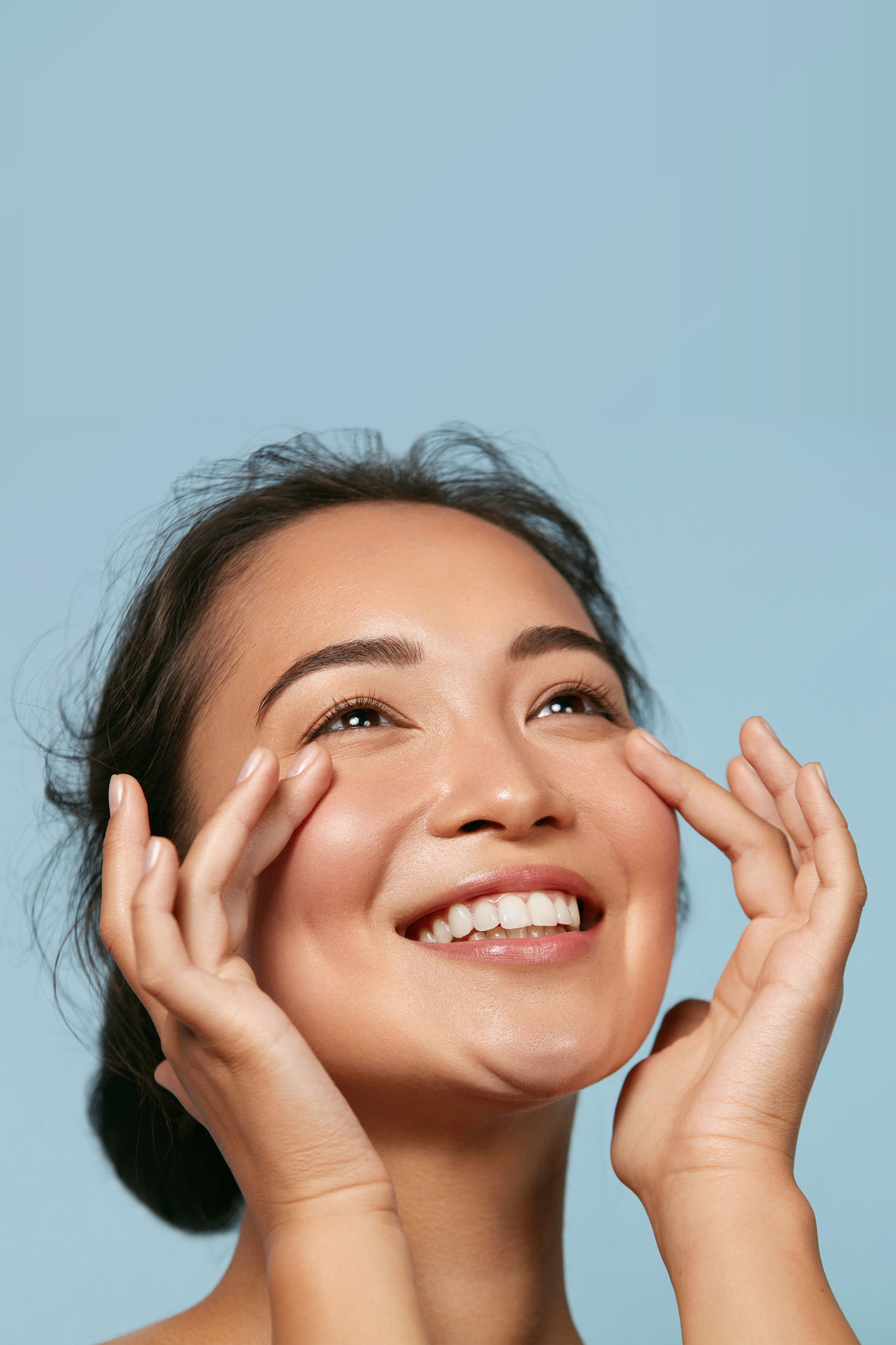 Smiling woman gently lifting her cheeks with her fingertips, showing full, smooth cheeks and under-eyes