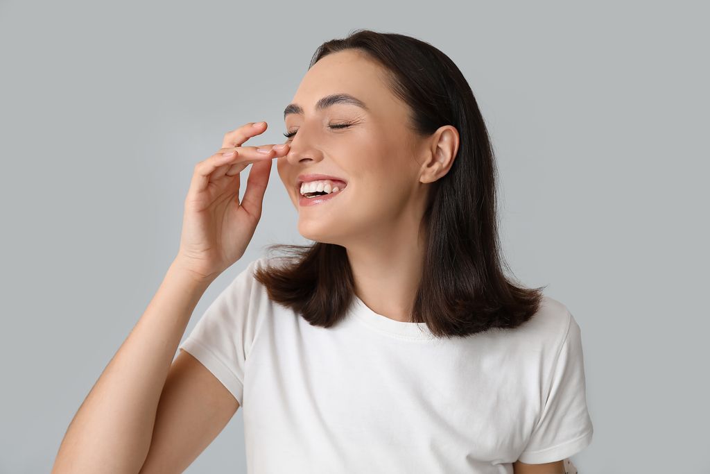 A smiling woman gently touches her nose, illustrating recovery and sensation after rhinoplasty on a blog about post-surgery h