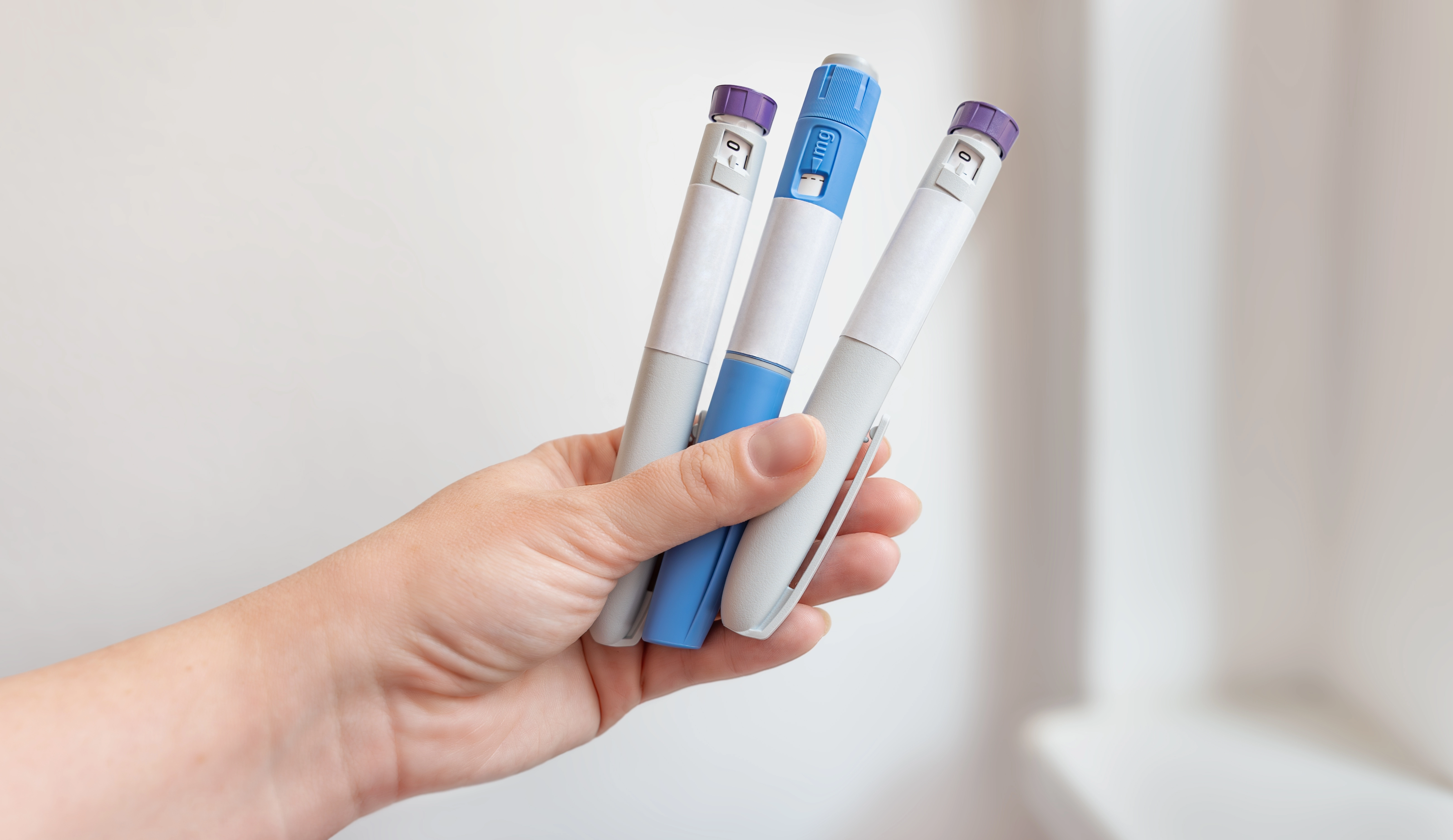 A hand holding three injectable medication pens used for weight loss or diabetes treatment.