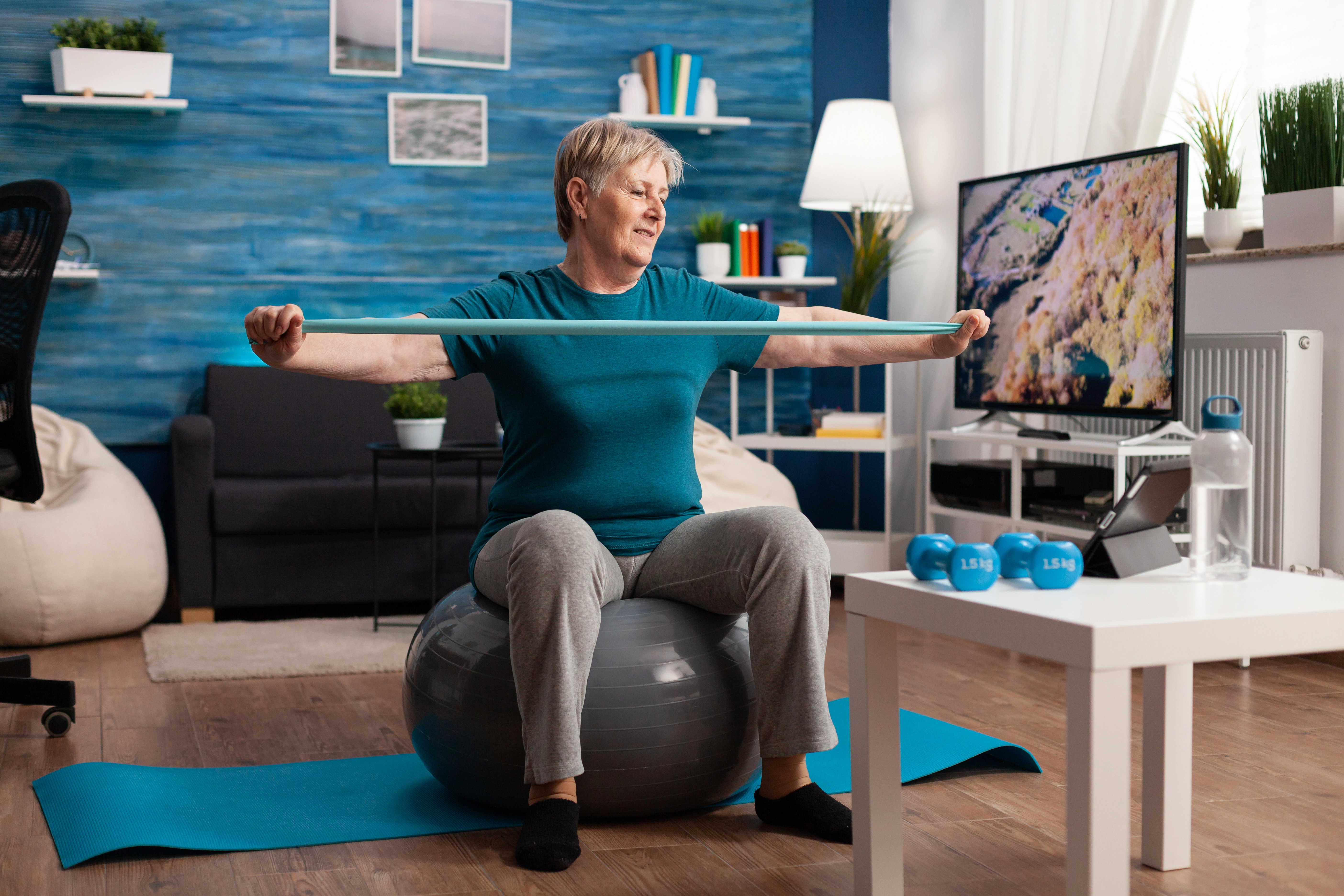 Older woman doing resistance band exercises while seated on a stability ball at home