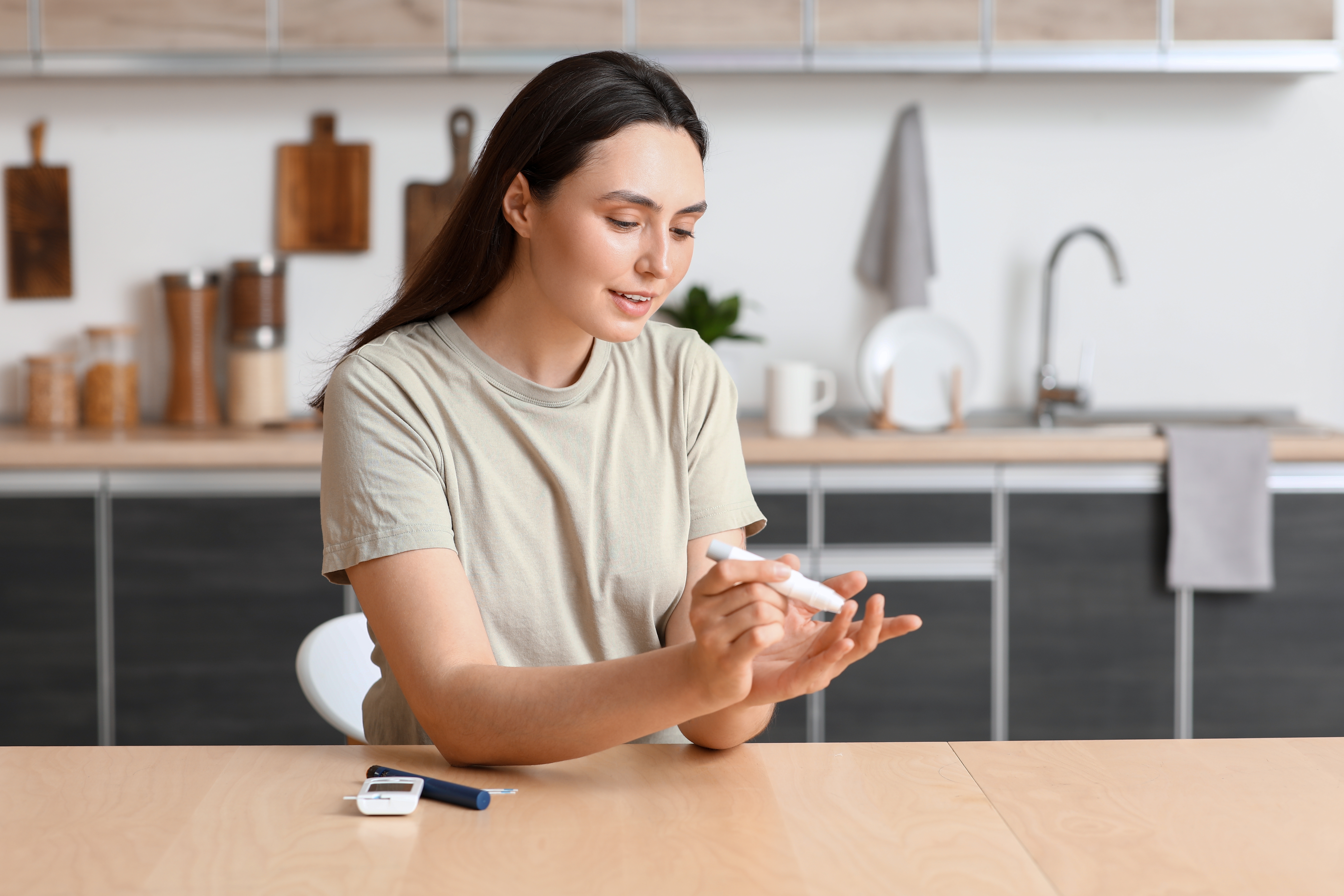 A woman sits at her kitchen table testing her blood sugar with a lancet device and glucose meter