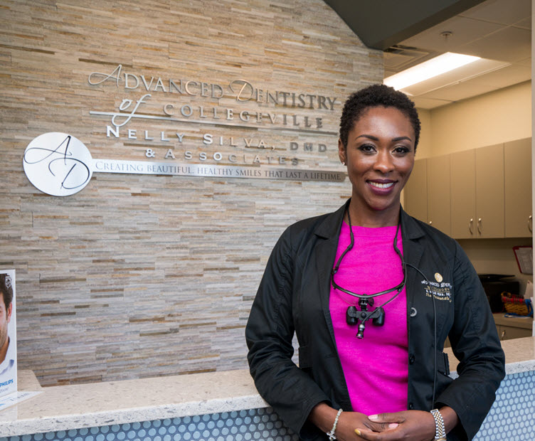 Dr. Nelly Silva smiling in front of the welcome wall at our Collegeville dental office