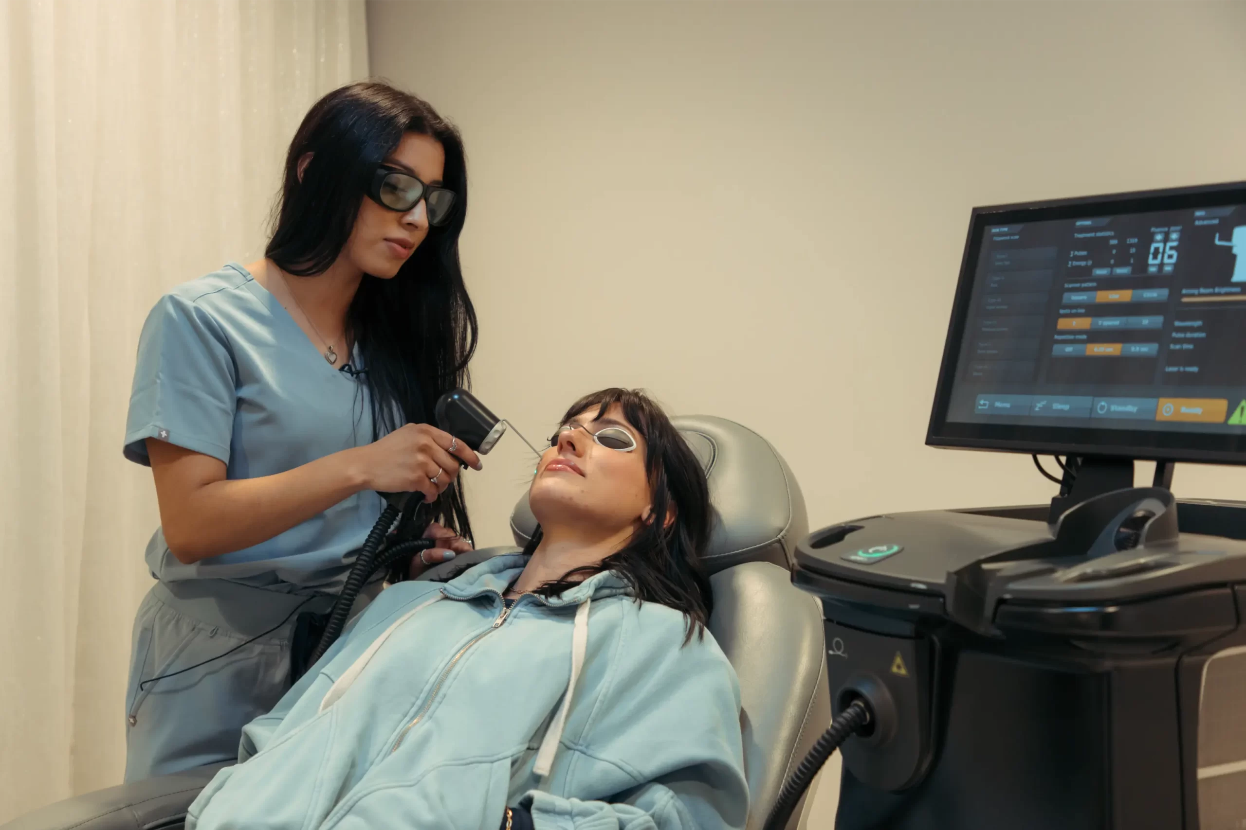 A medspa provider performs a laser treatment on a reclined patient wearing protective eyewear in a treatment room