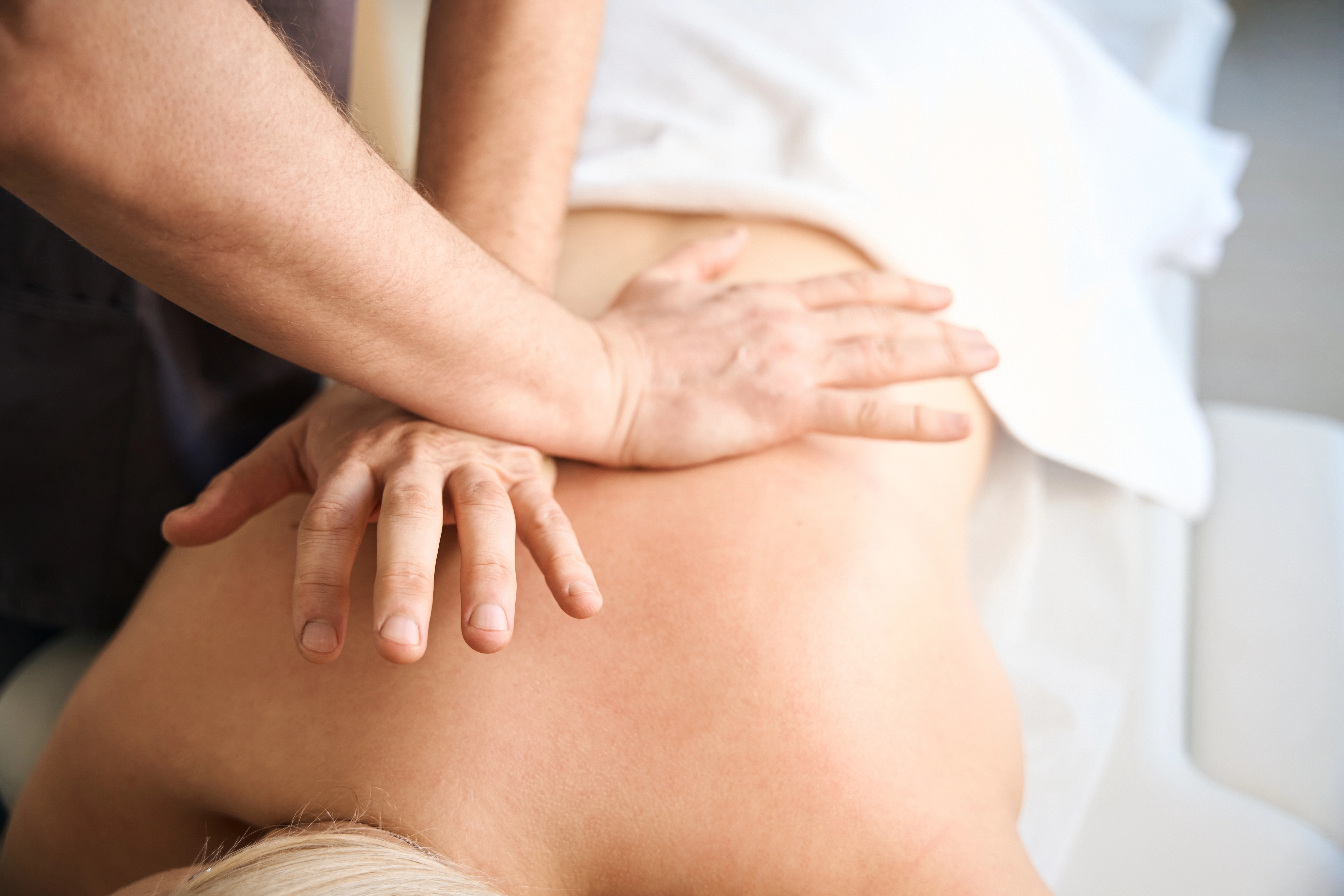 Therapist's hands applying myofascial release to a patient's upper back on a treatment table