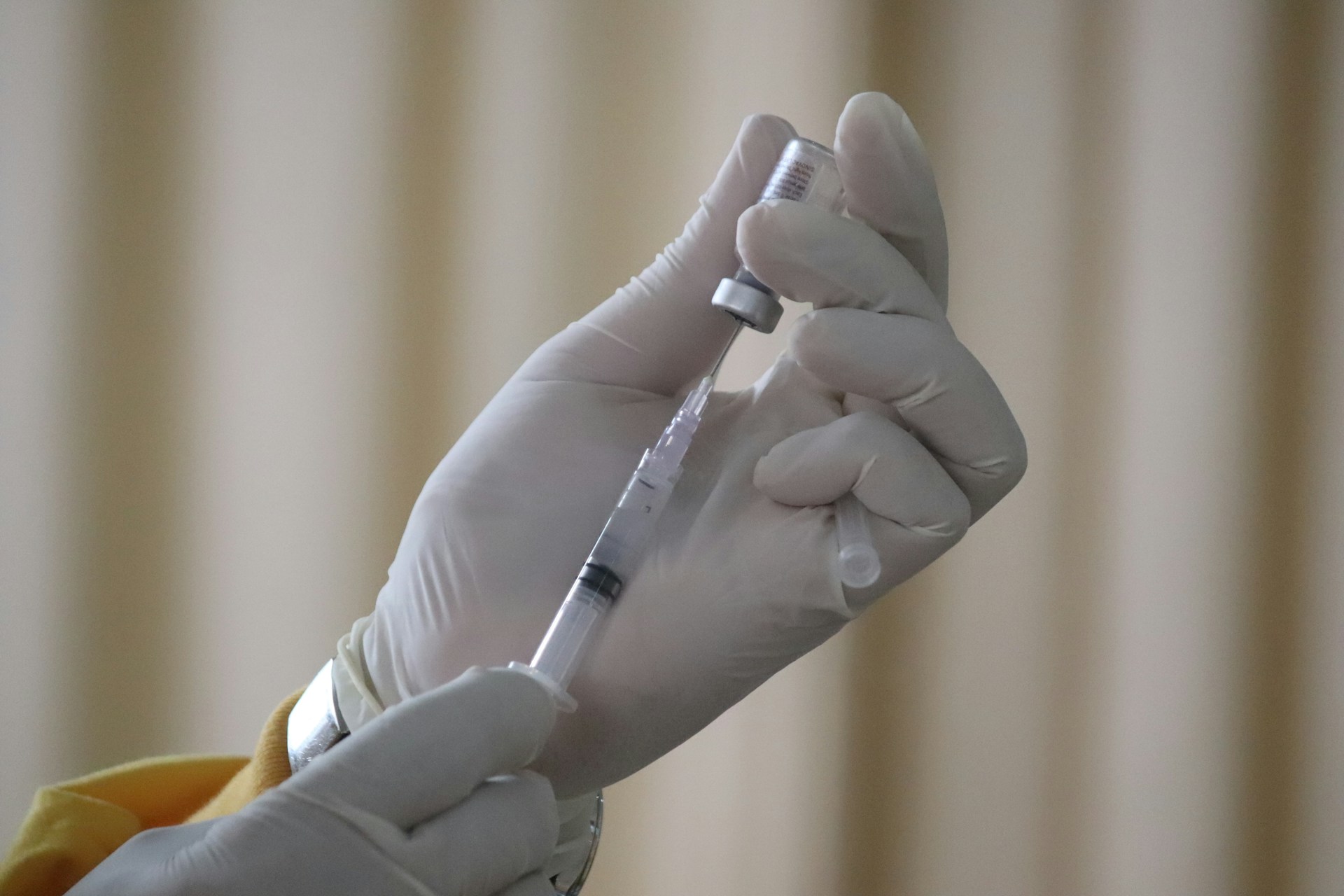 Gloved hands drawing an injection solution from a glass vial into a syringe