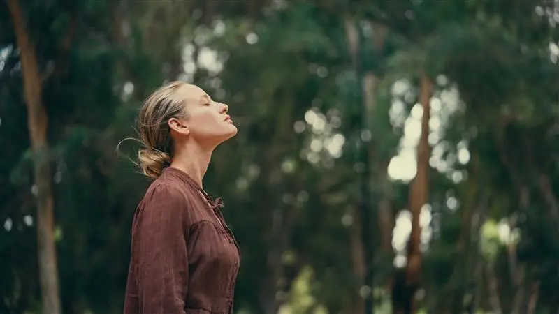 Stock photo of a woman with eyes closed breathing deeply outdoors among trees, used as a banner for an article about balloon