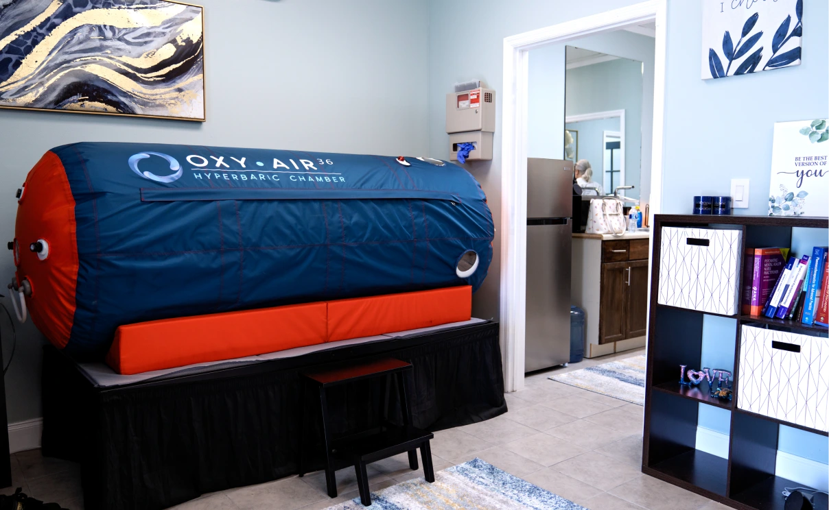 An office room featuring a hyperbaric oxygen therapy chamber with branded shelving and decor in the background