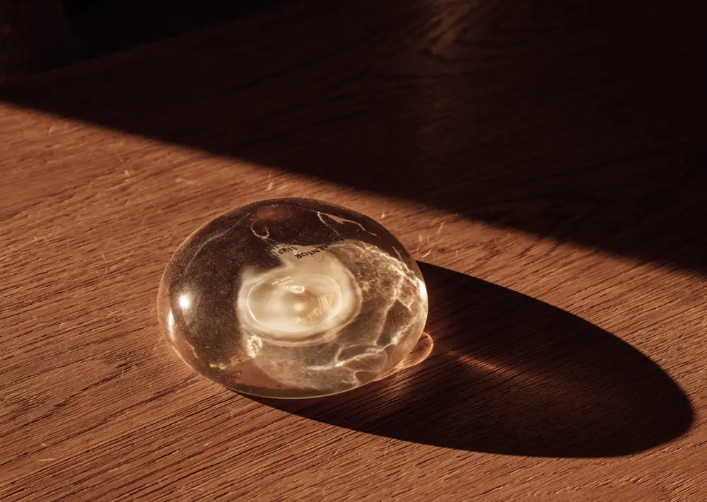 A silicone breast implant sitting on a wooden surface, lit dramatically by a shaft of sunlight