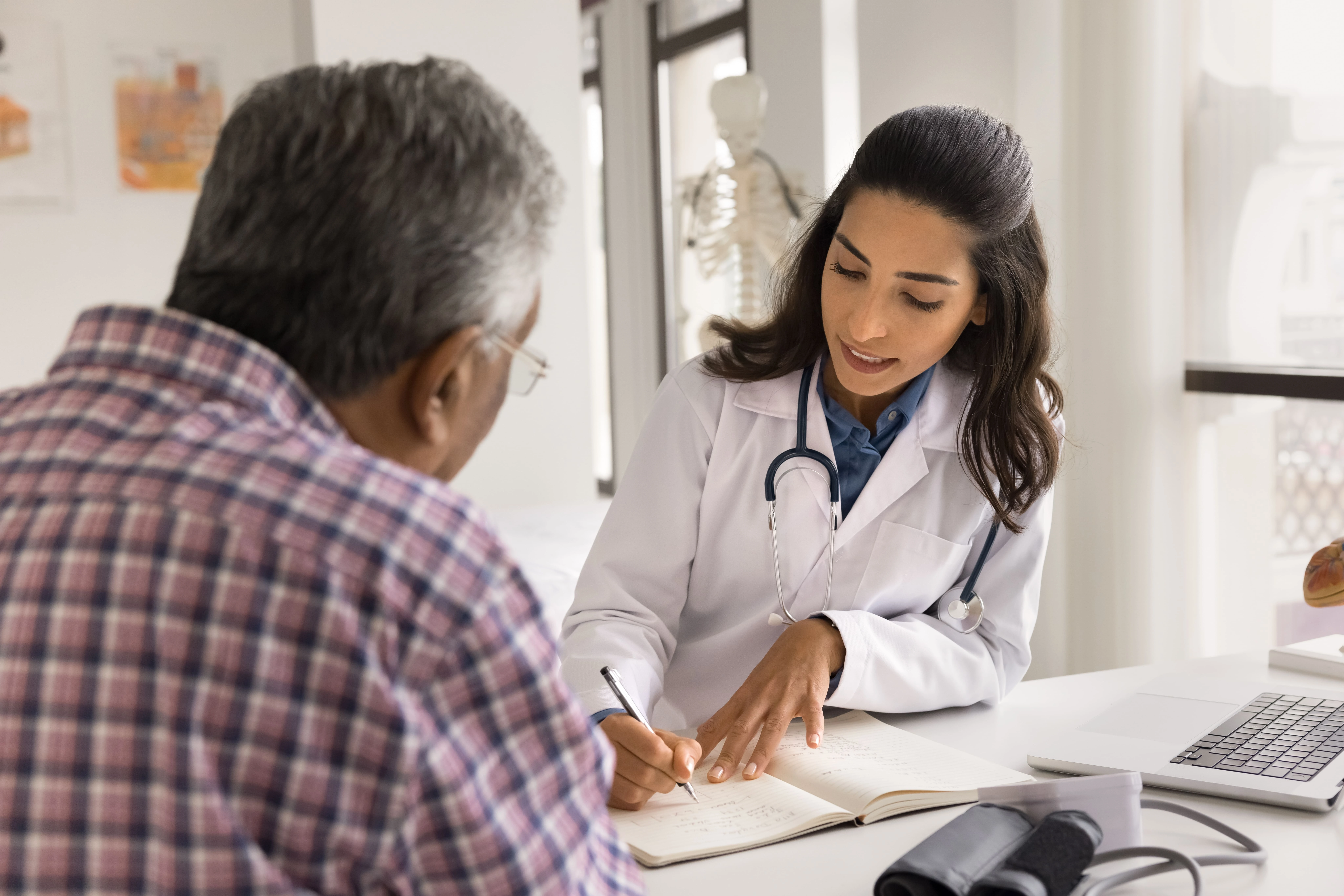 A doctor in a white coat reviews notes with a patient during a consultation