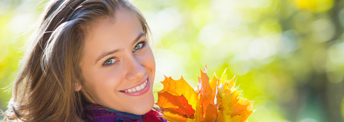 Smiling woman with bright white teeth in warm autumn light, illustrating KöR teeth whitening