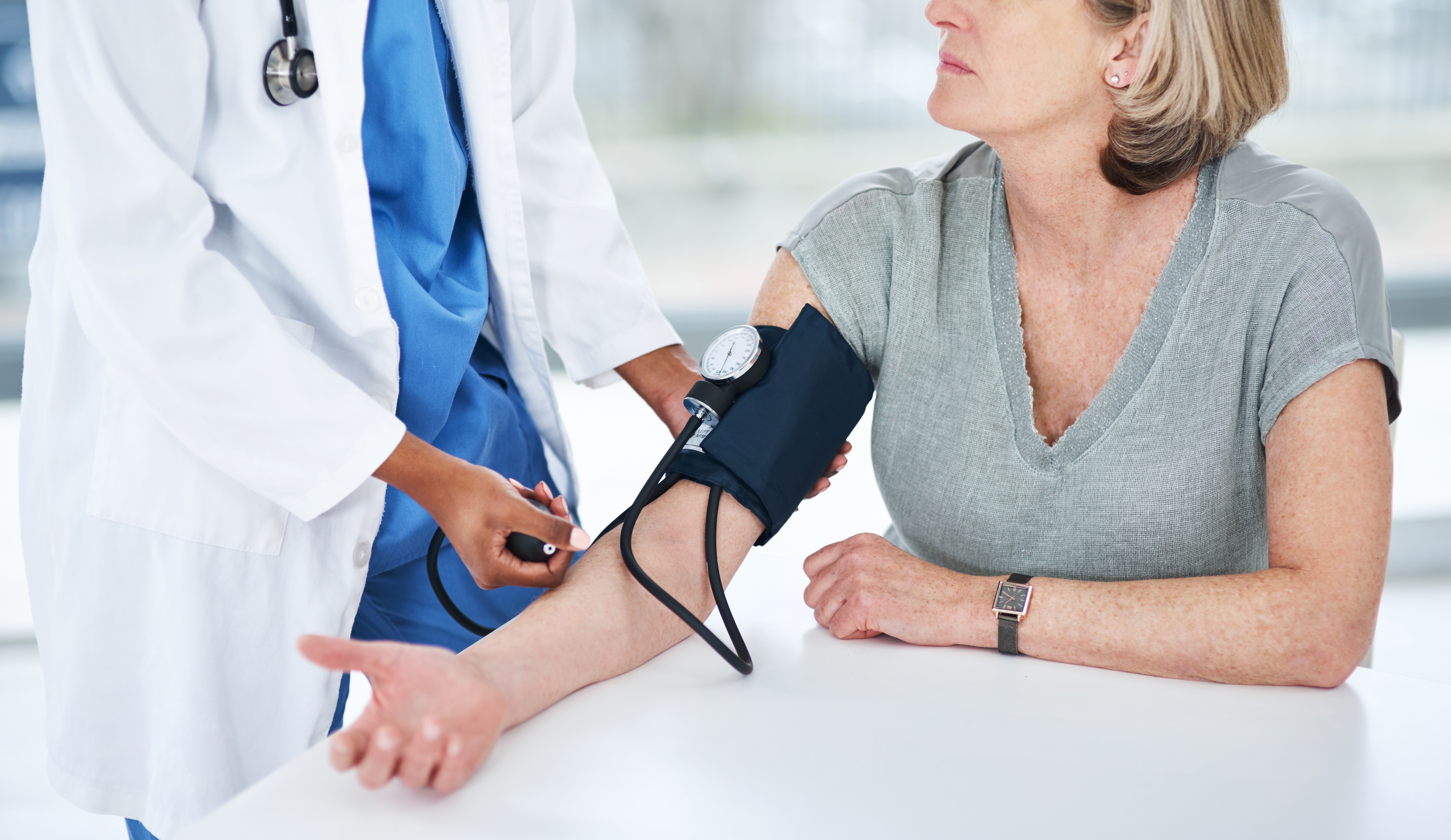 A doctor measures an older woman's blood pressure with a manual cuff during a checkup