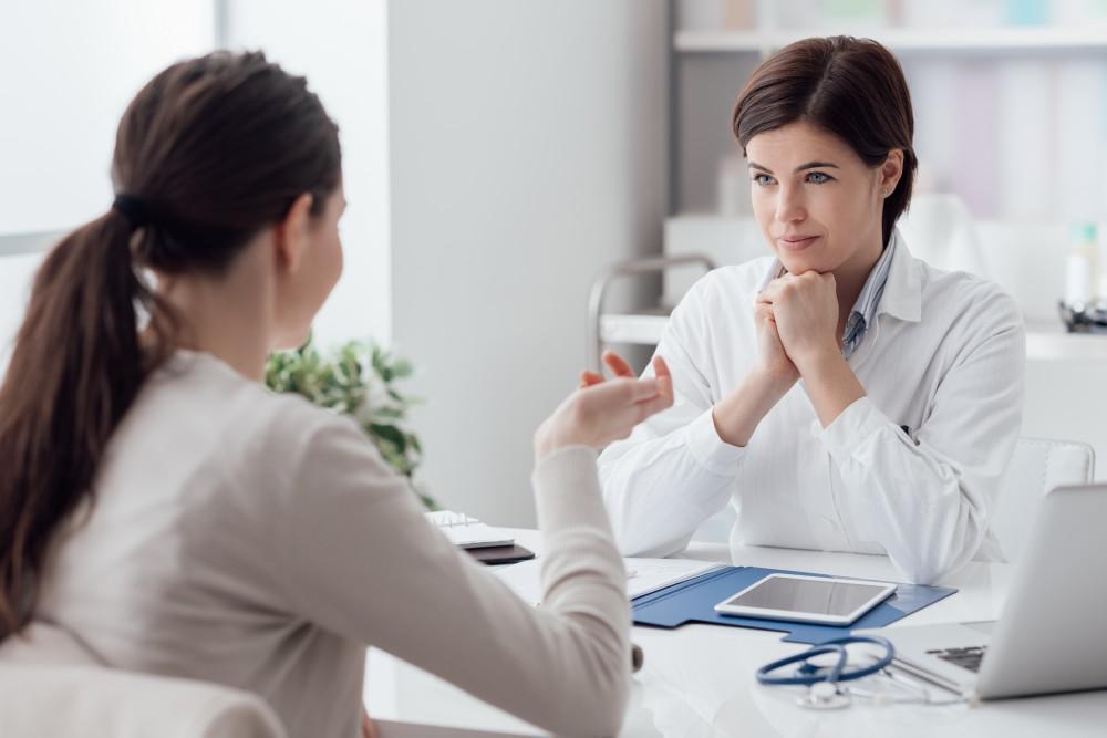 Stock photo of a female doctor in a white coat listening attentively to a patient during a consultation, used to illustrate a blog post about ketamine treatment.