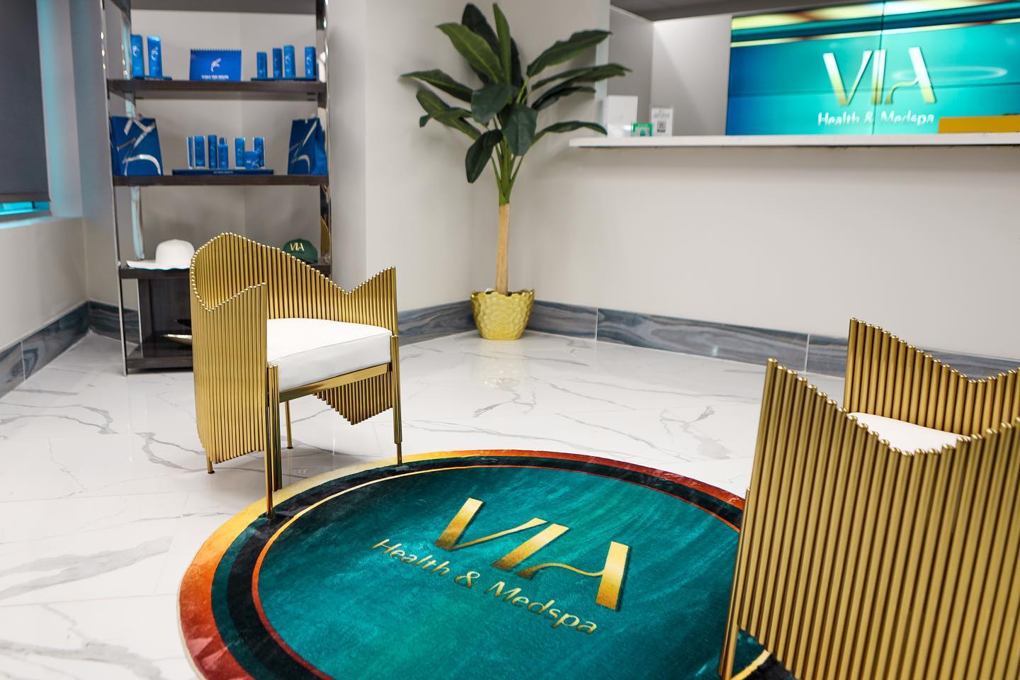 Reception area at VIA Health & Medspa in Chandler with gold accent chairs and the VIA logo rug