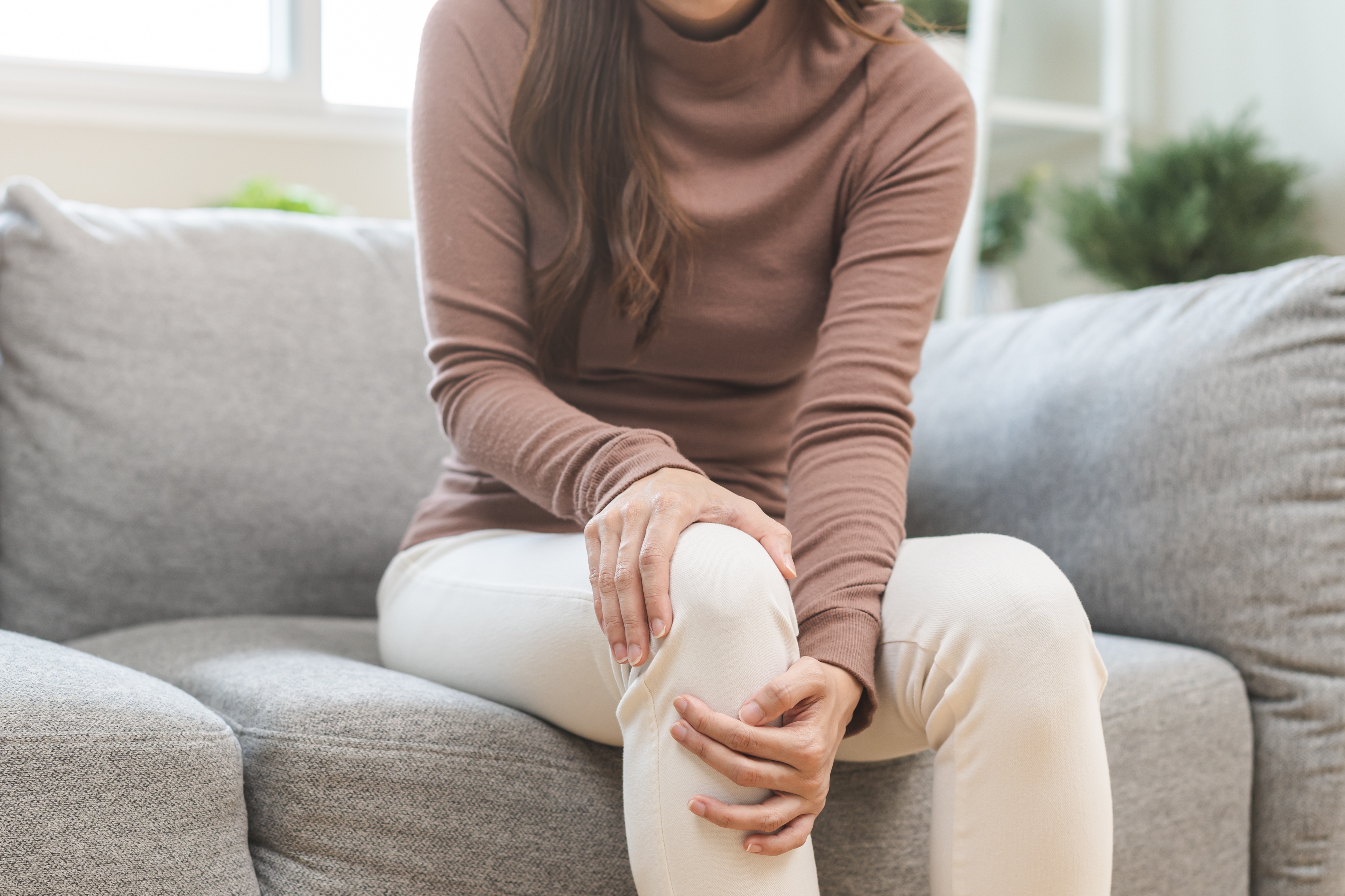 Woman seated on a grey sofa holding her knee with both hands