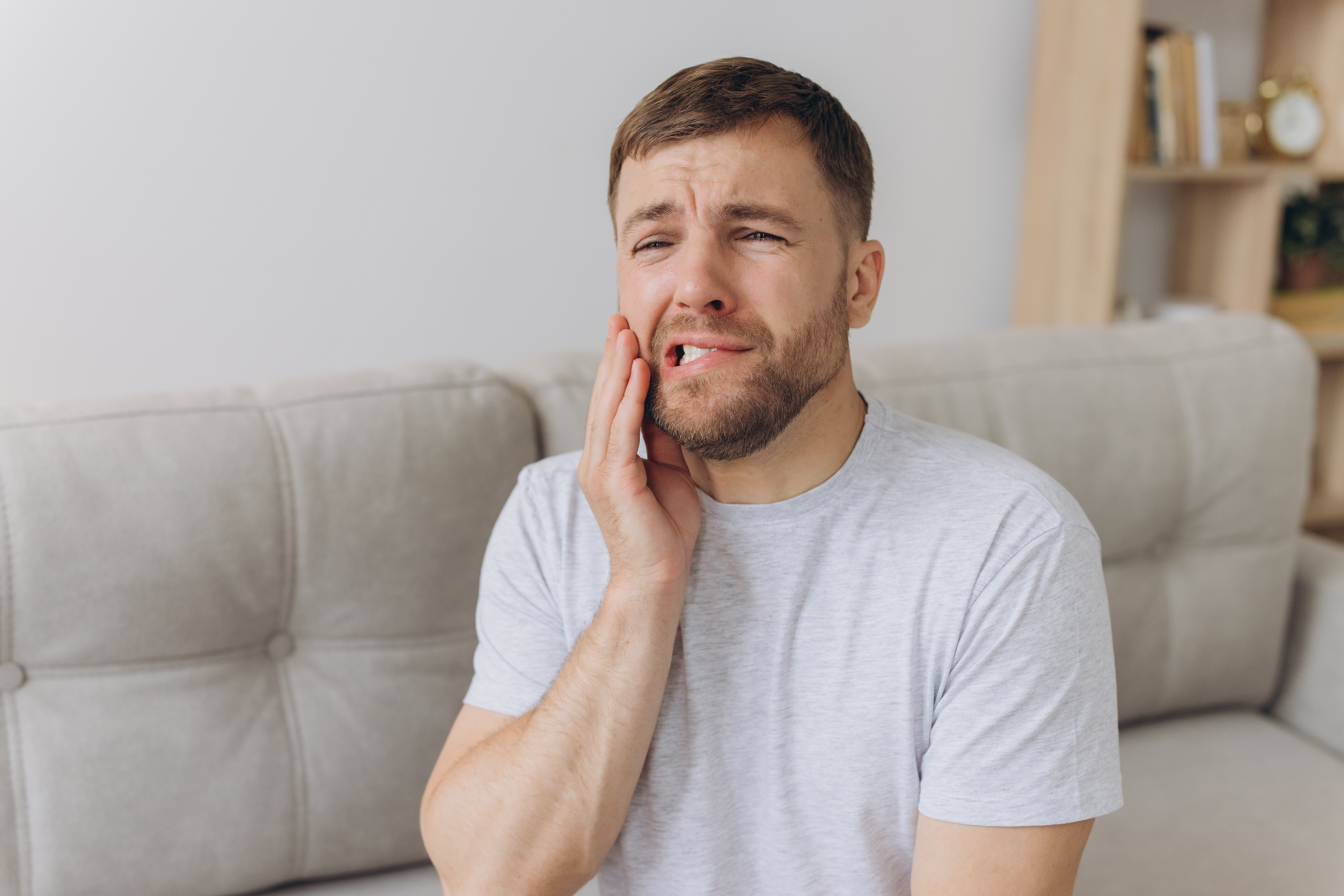 A man winces in pain while touching his jaw, illustrating a broken, cracked, or chipped tooth emergency for a dental care gui