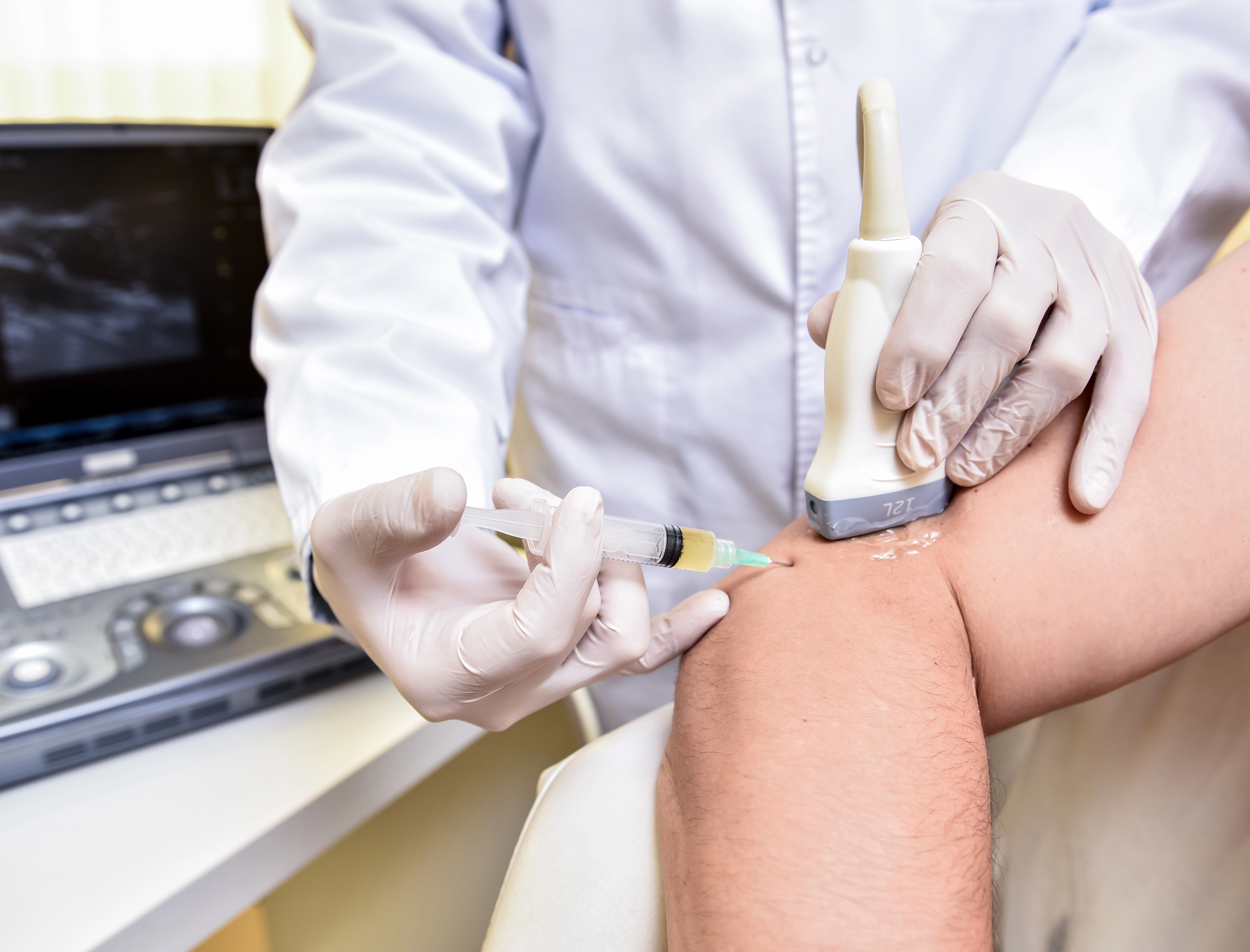 Clinician in gloves giving an injection beside a patient's knee in a treatment room
