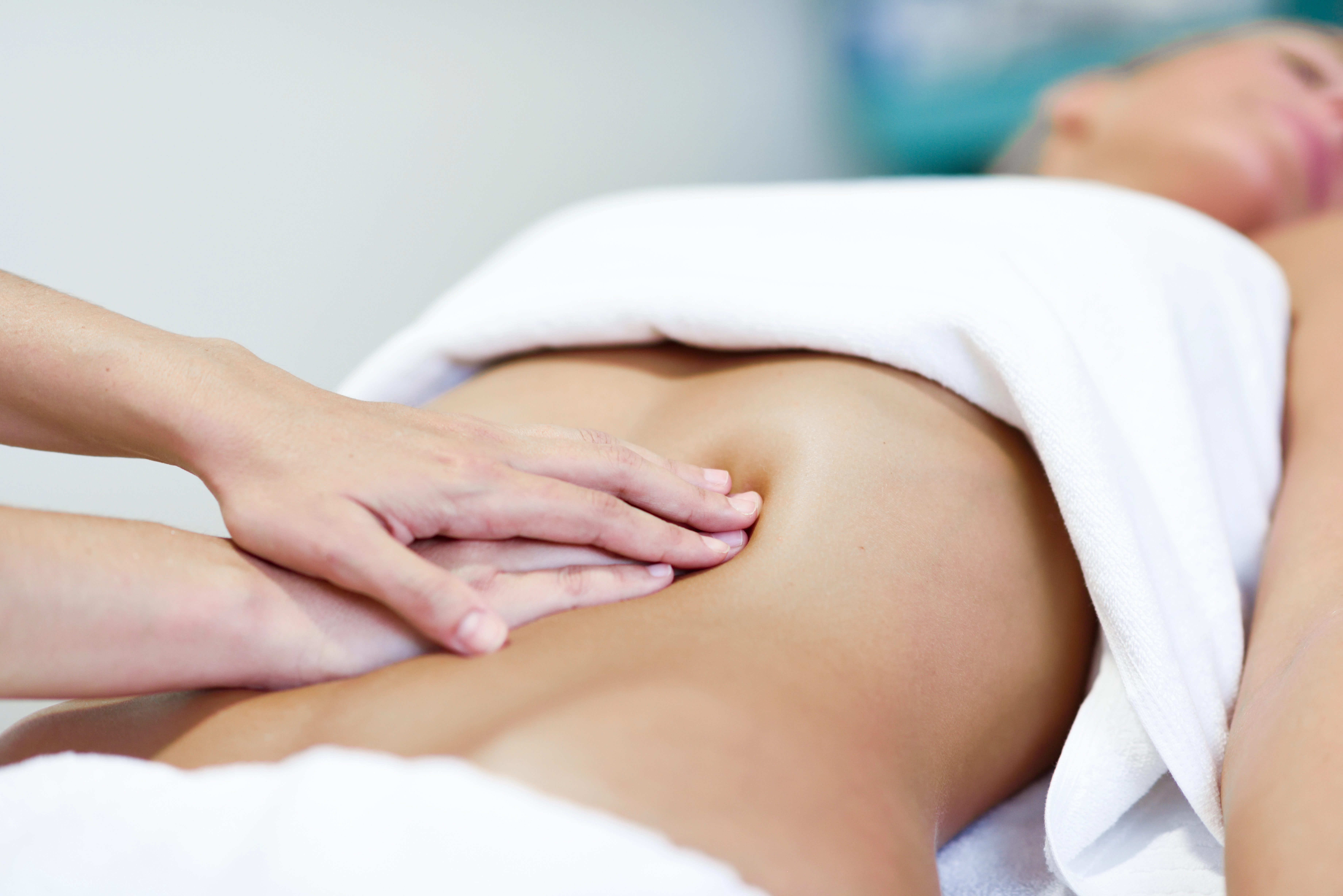 Gentle hands-on lymphatic work over a patient's abdomen on a treatment table with white towels