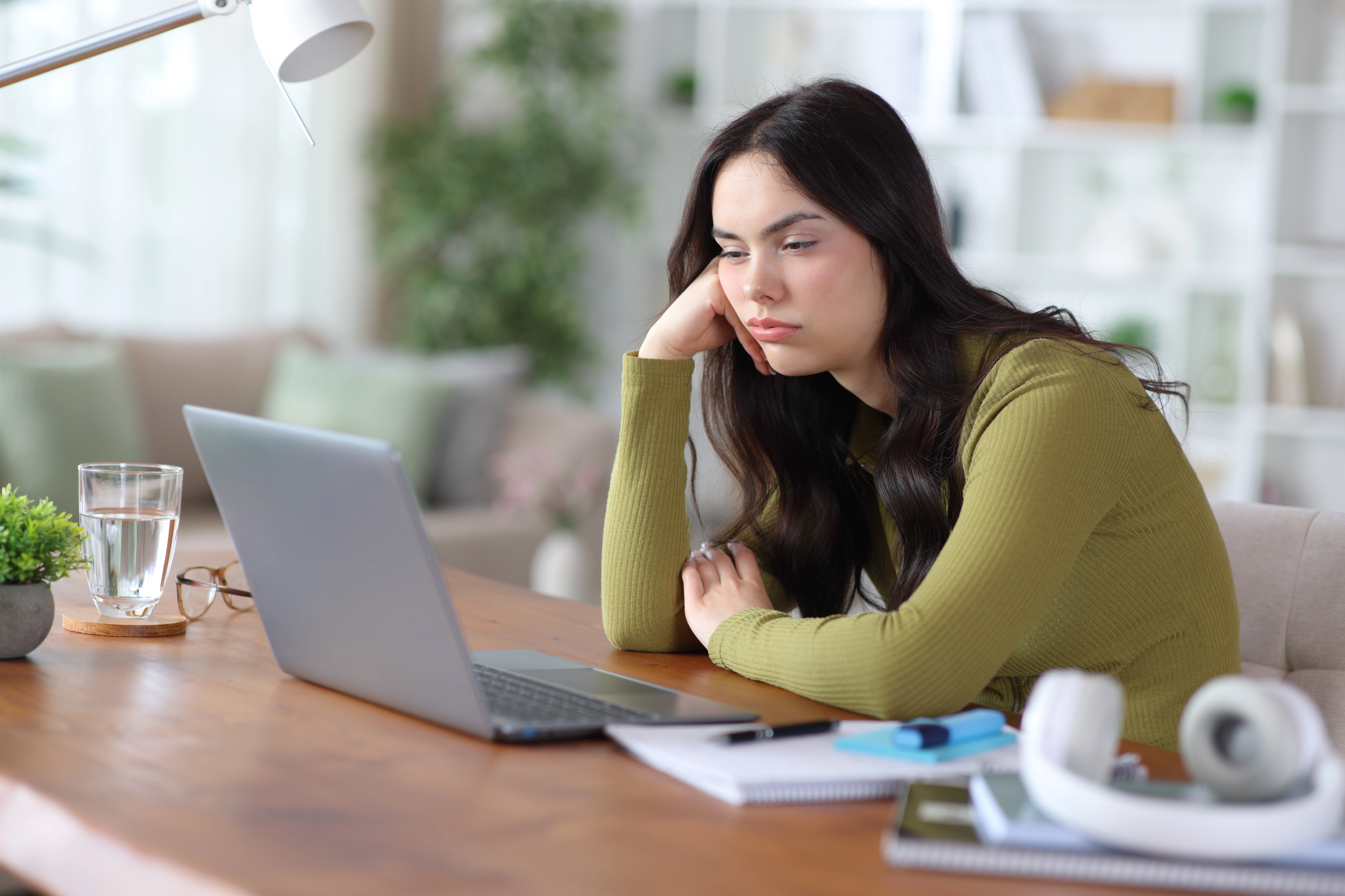 A young woman looks tired and distracted while sitting at a desk with a laptop in a home setting, illustrating a blog post ab