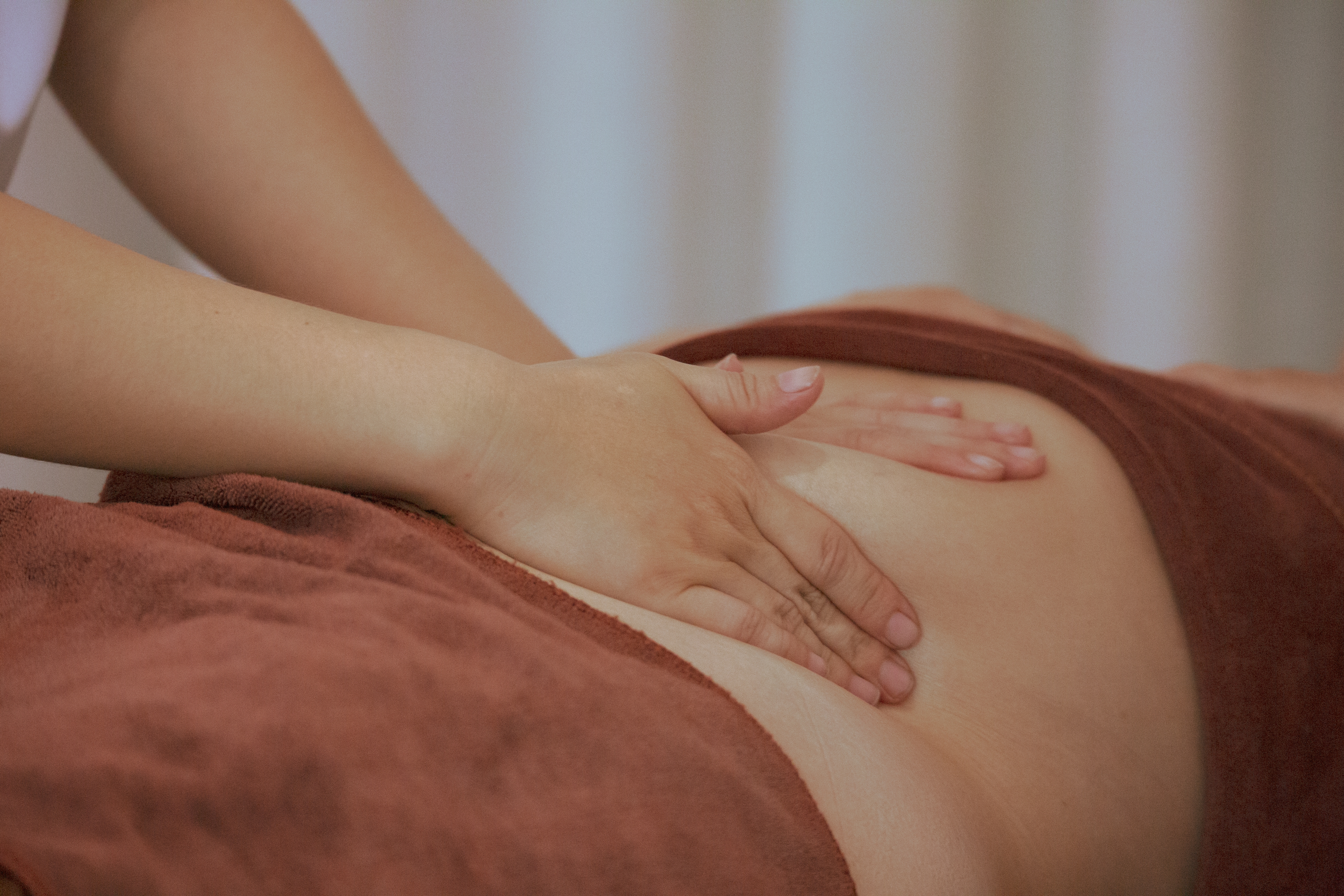 Gentle hands-on lymphatic work over the abdomen of a patient resting under a towel
