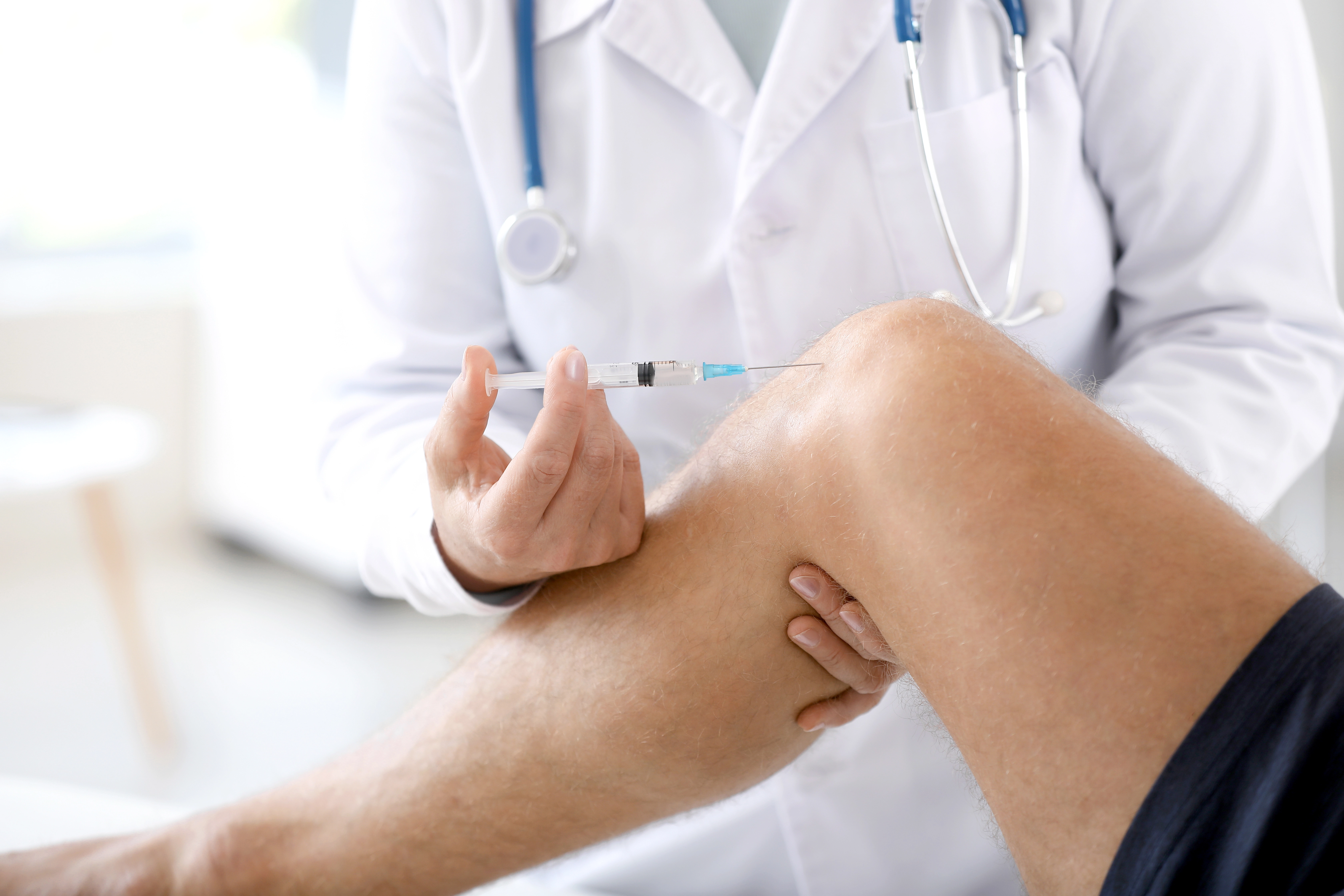 Clinician in a white coat giving an injection into the side of a patient's knee