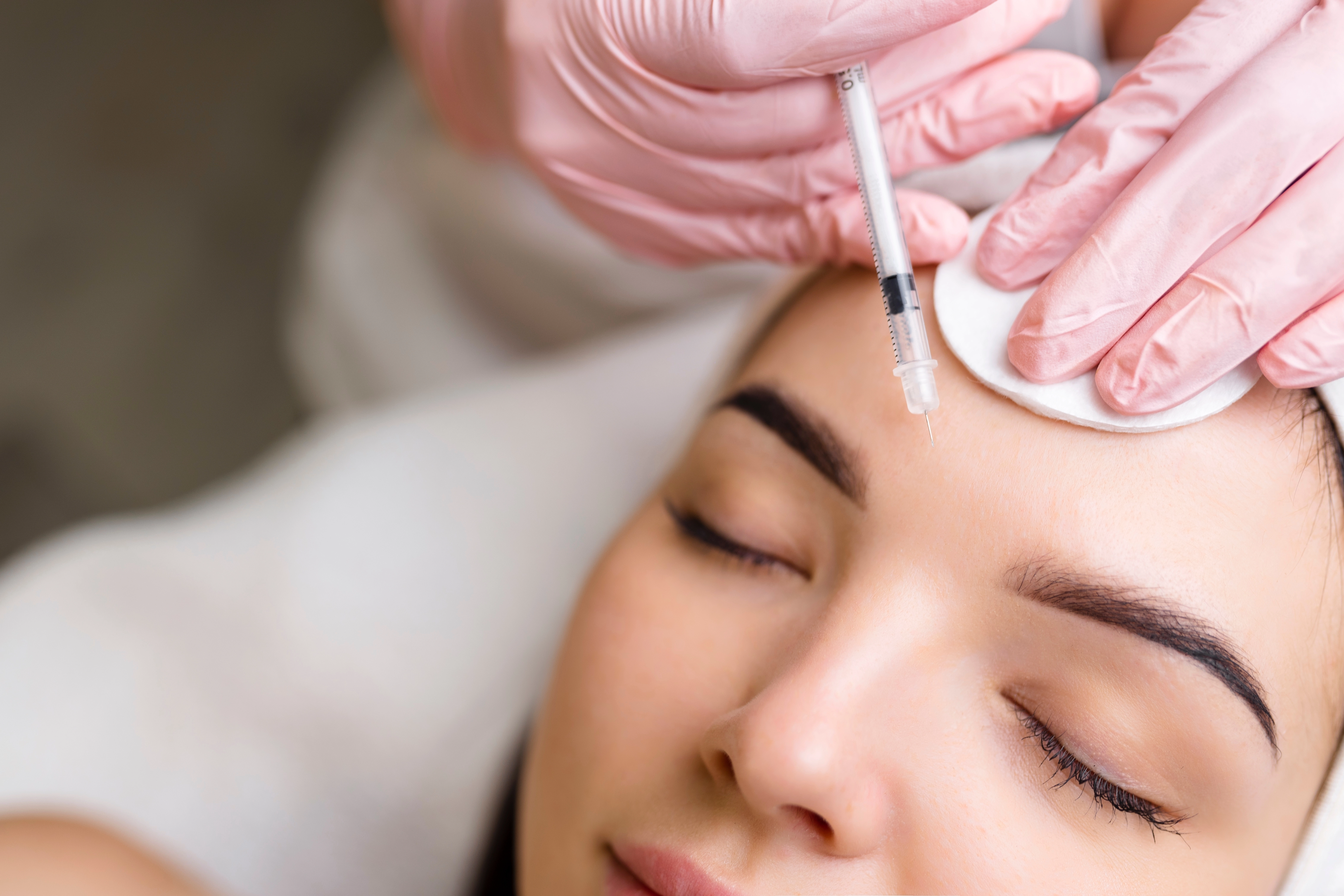 A gloved cosmetologist administers a botox injection into a woman's forehead to treat frown lines
