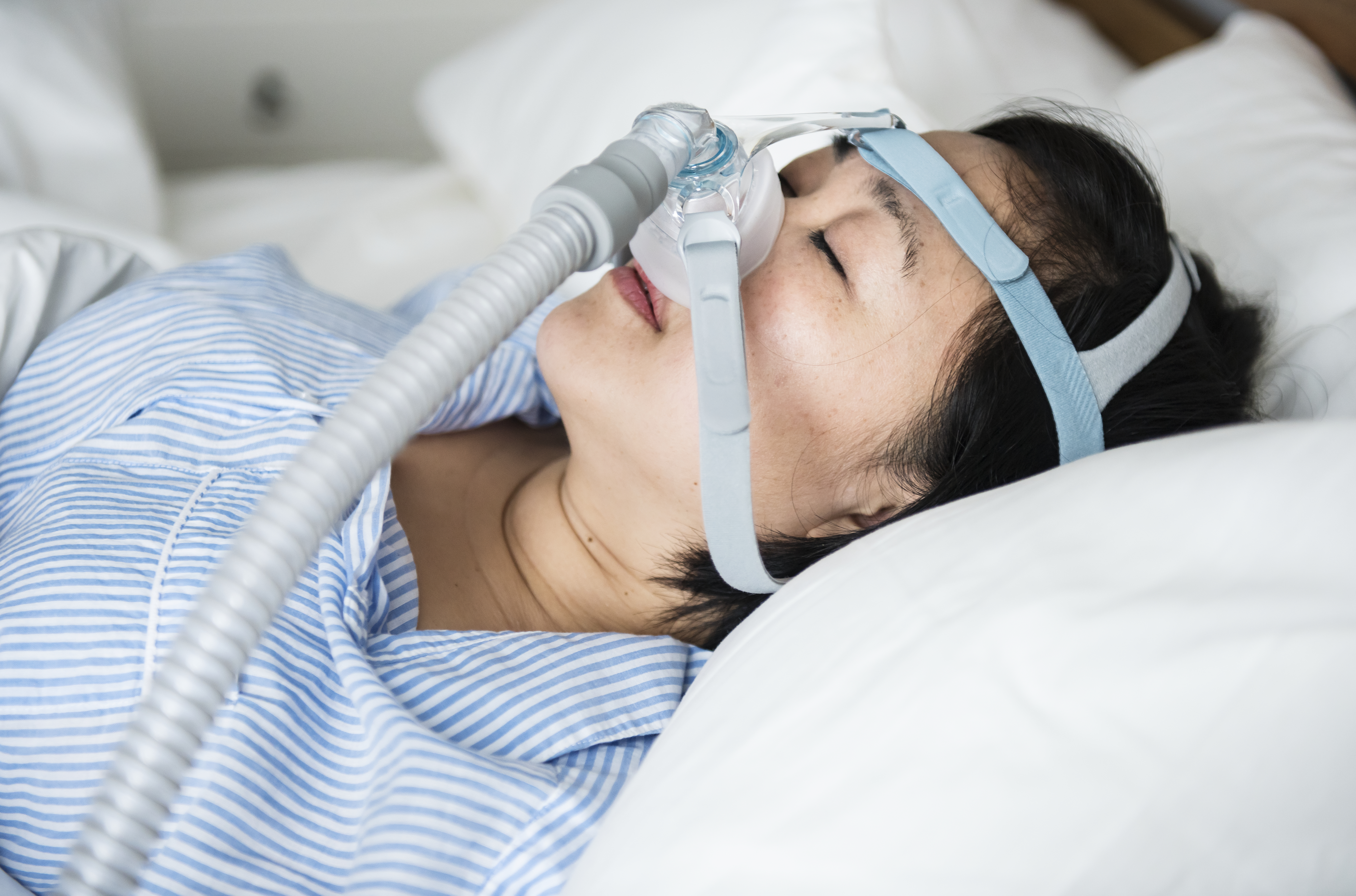A woman sleeps in bed while wearing a CPAP mask to treat sleep apnea